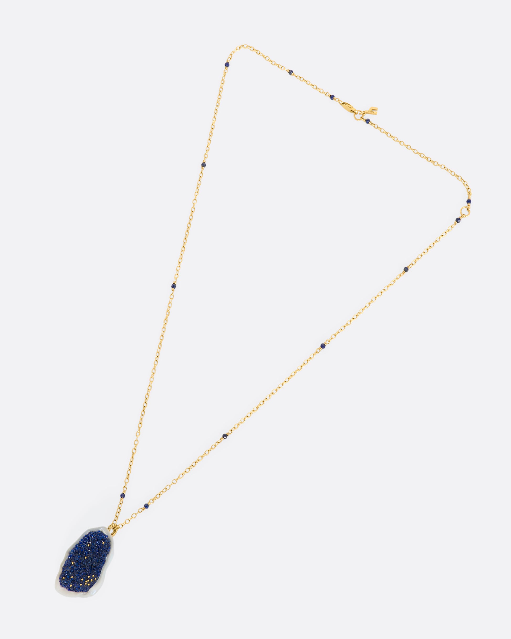 A yellow gold necklace with a hollowed out pearl pendant filled with lapis and 22k gold beads. Shown laying flat.