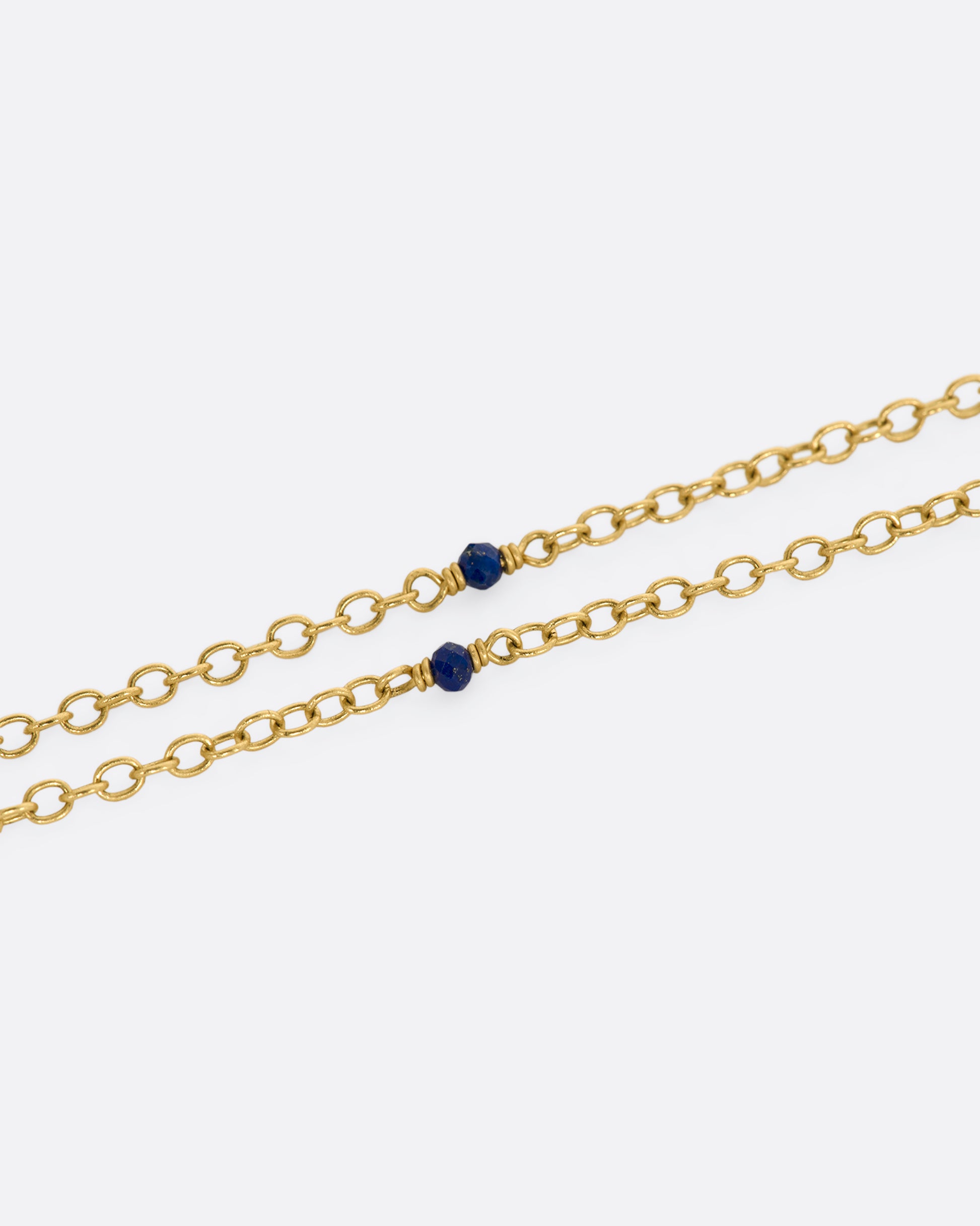 A yellow gold necklace with a hollowed out pearl pendant filled with lapis and 22k gold beads. Shown close up of the lapis beads on the chain.
