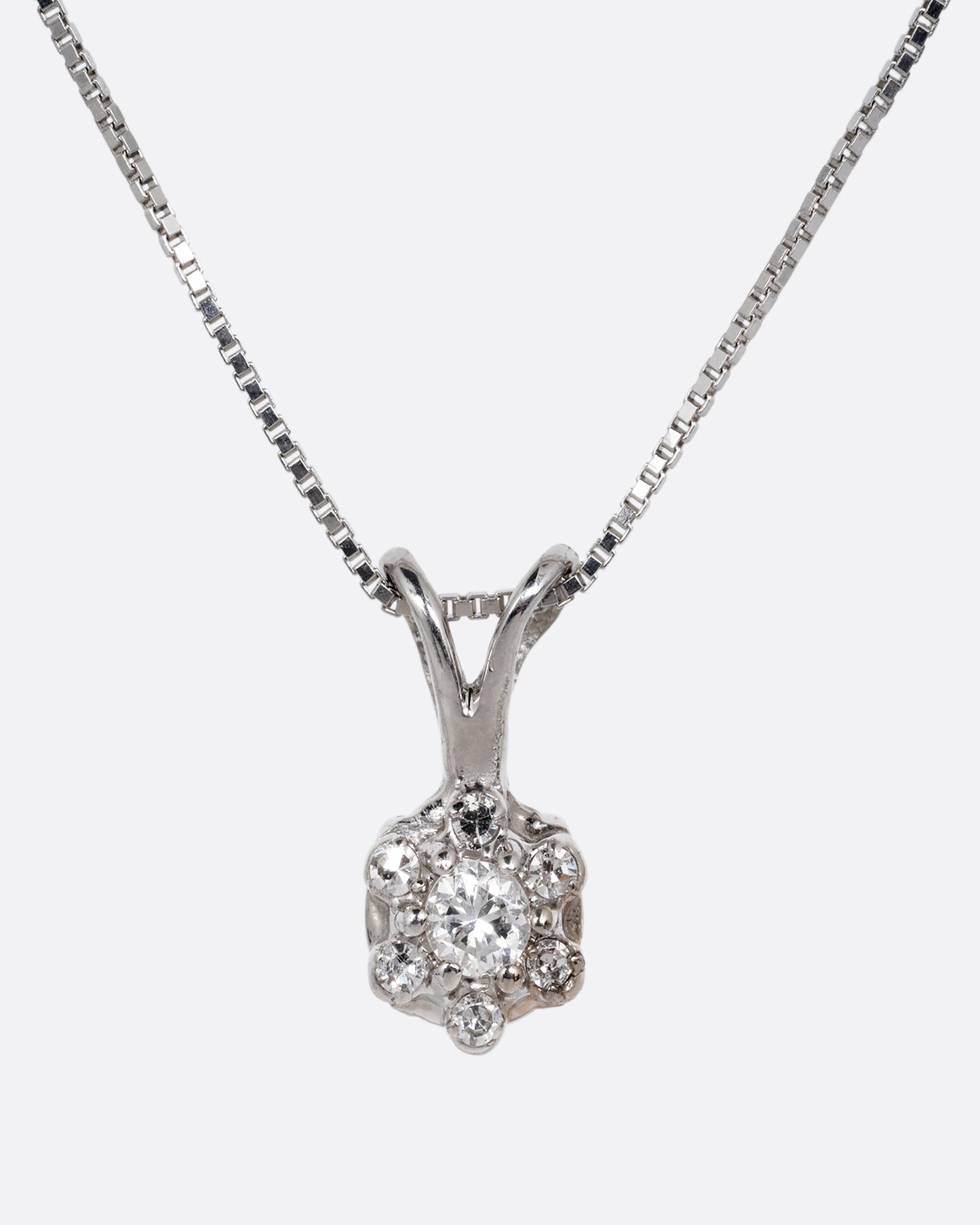A white gold box chain necklace with a diamond studded flower shaped pendant. Shown from the front.