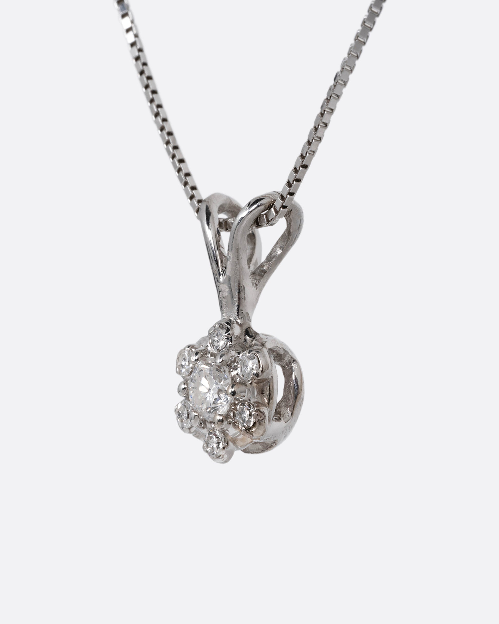 A white gold box chain necklace with a diamond studded flower shaped pendant. Shown from the side.