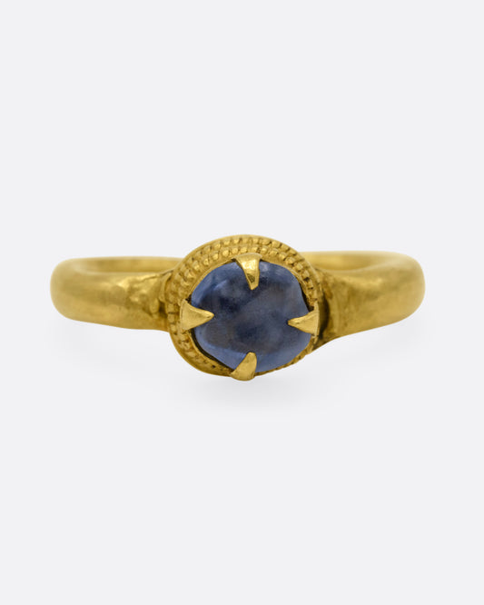 An ancient yellow gold ring featuring a prong set central cornflower-blue sapphire, shown from the front.