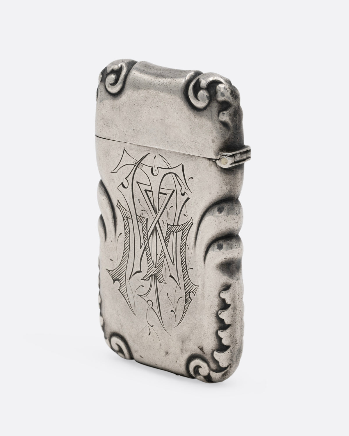 A silver match safe with a deer among scroll work, shown from the side.