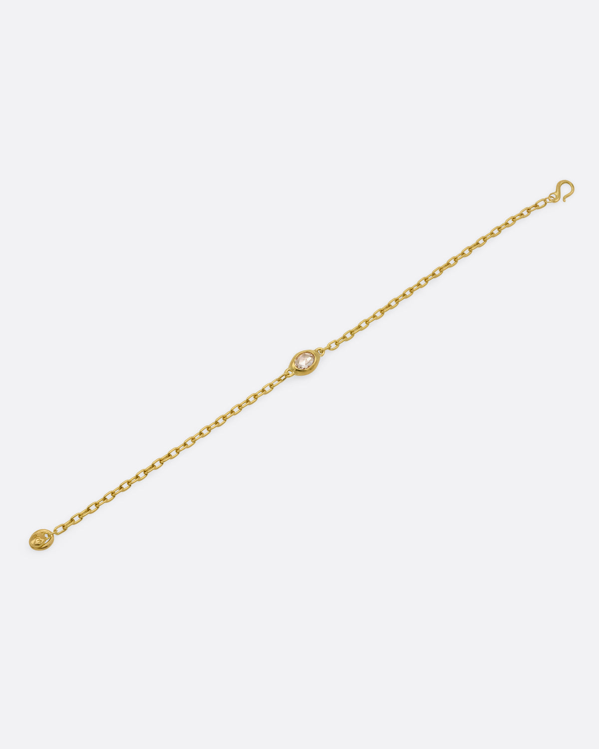 A yellow gold cable chain bracelet with an oval rose cut diamond in a chunky bezel setting, shown from the front. 