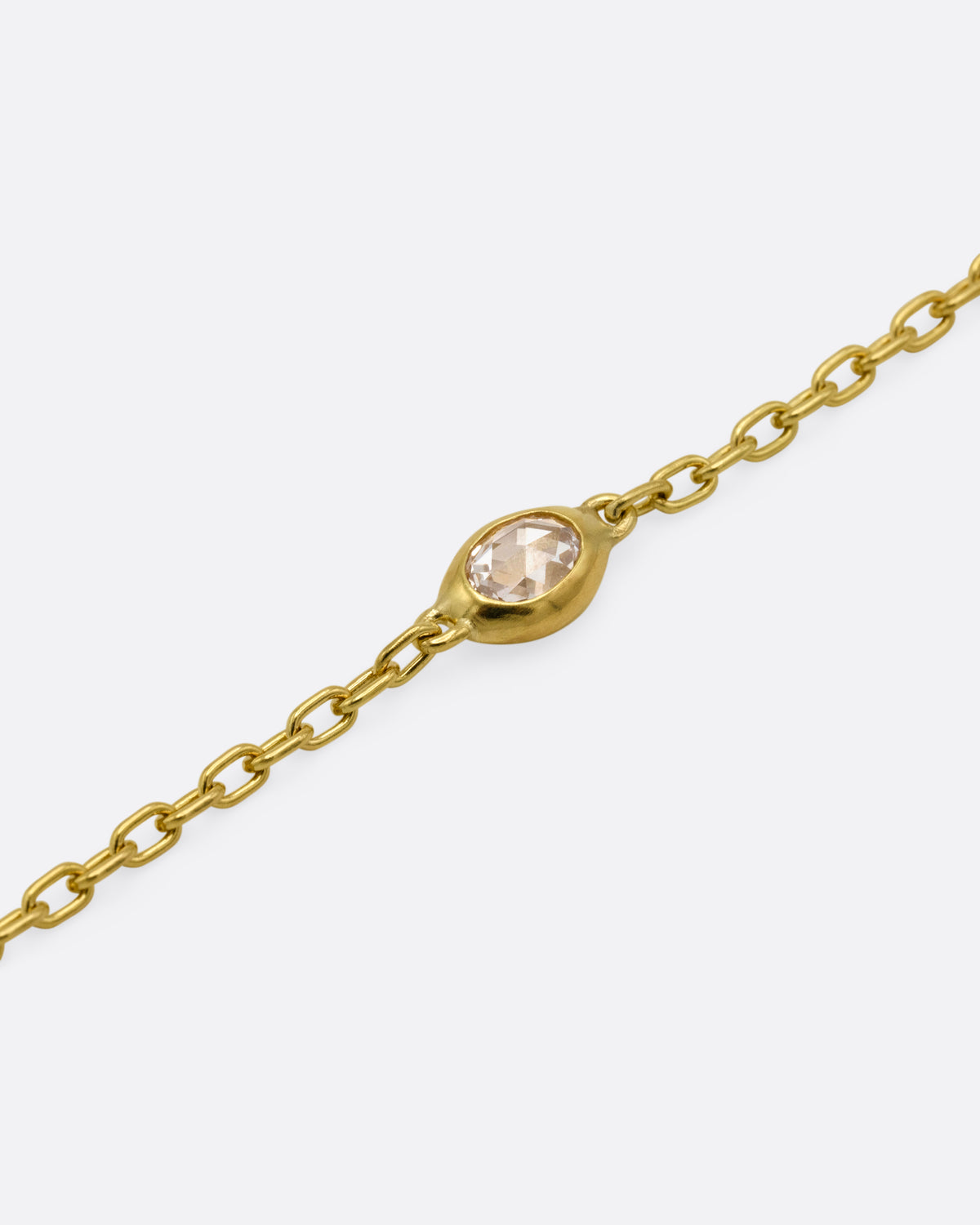 A yellow gold cable chain bracelet with an oval rose cut diamond in a chunky bezel setting, shown from the front. 