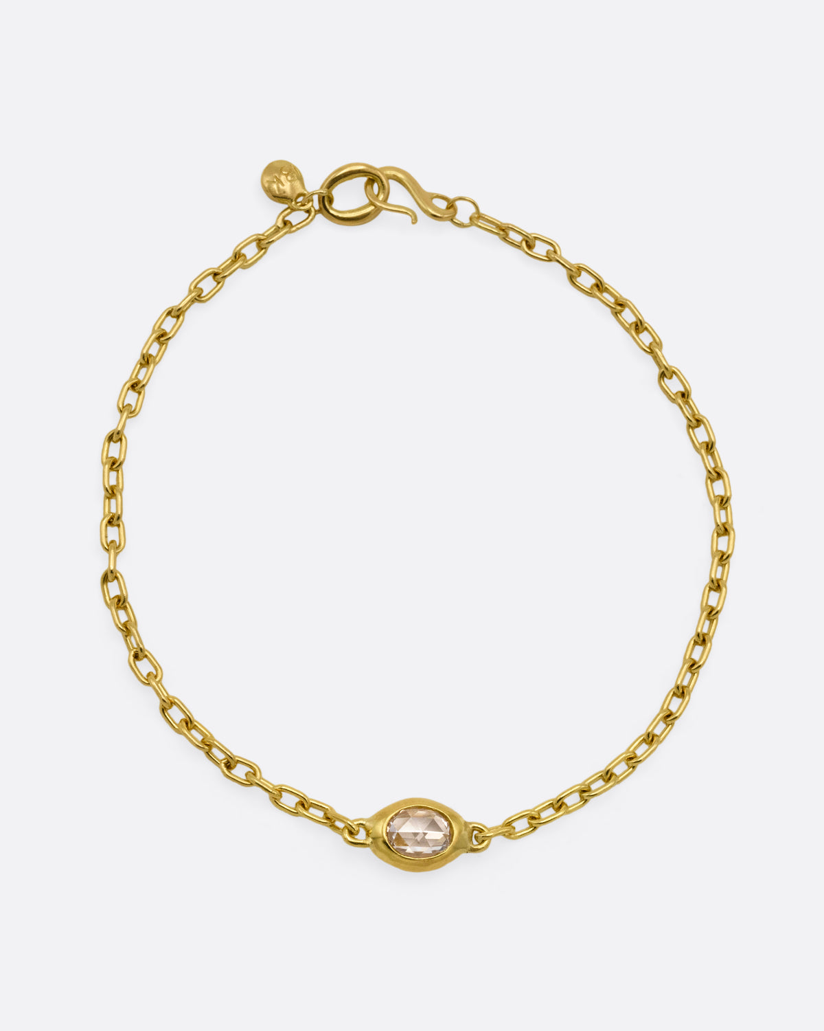 A yellow gold cable chain bracelet with an oval rose cut diamond in a chunky bezel setting, shown from the front. 