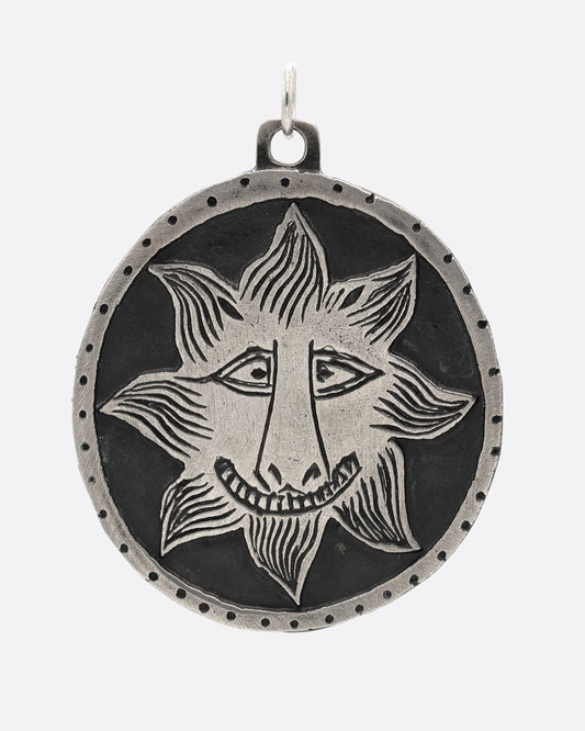 A silver medallion pendant with a smiling sun at the center. Shown from the front.