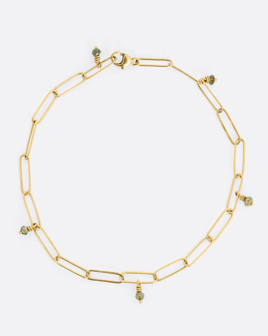 A bird's eye view of a yellow gold bracelet with popsicle stick-shaped links and green diamond beads scattered throughout. 