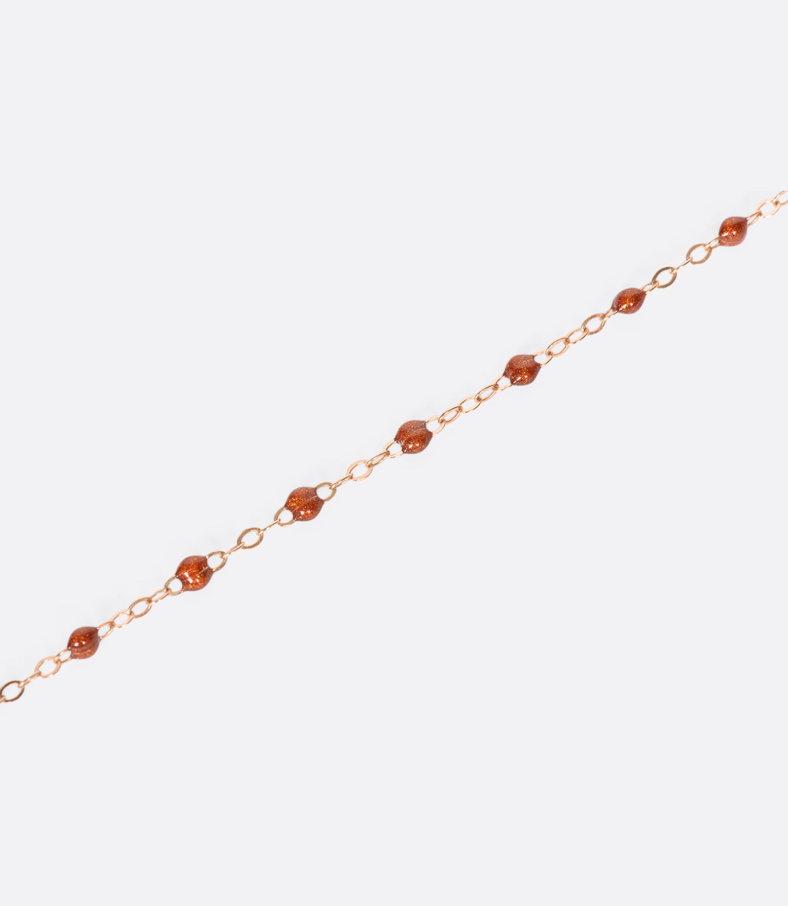 A close up view of a yellow gold cable chain necklace with rusty red resin droplets. Shown from the side.