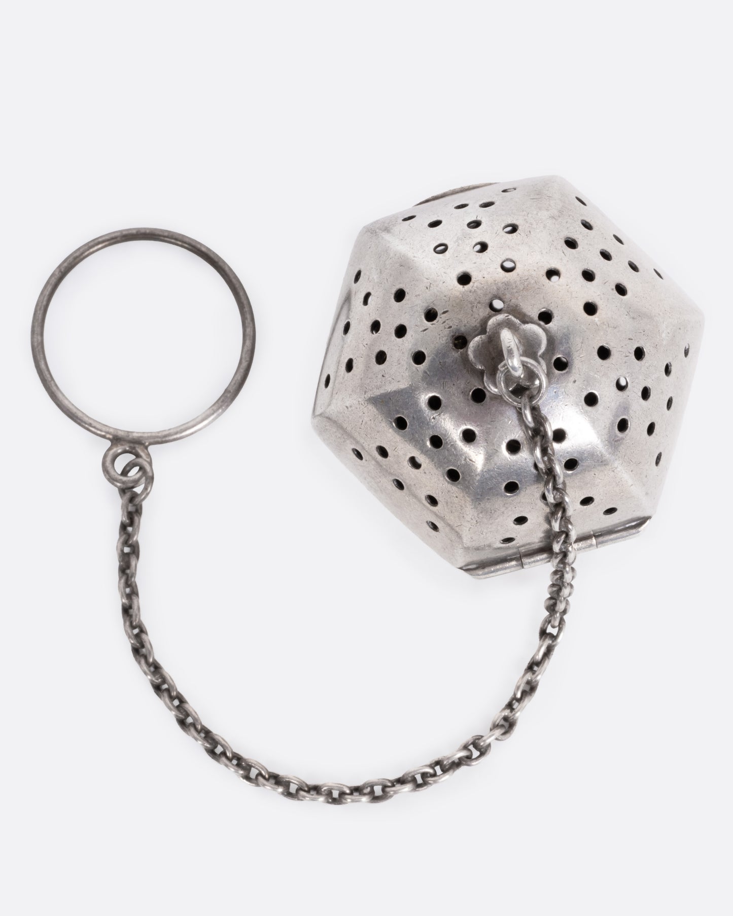 A hexagonal silver tea infuser with a chain, shown from the top.
