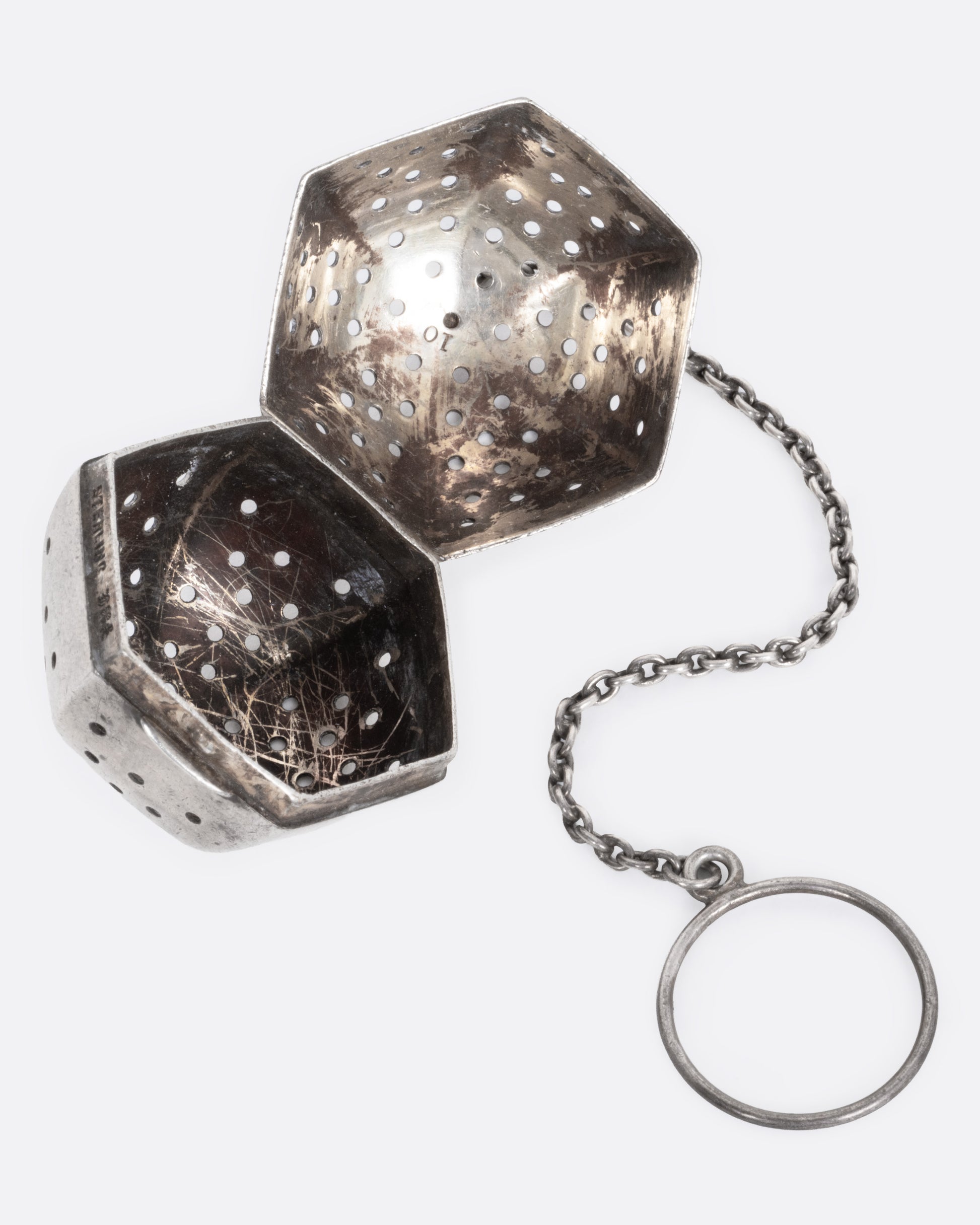A hexagonal silver tea infuser with a chain, shown open from the side.
