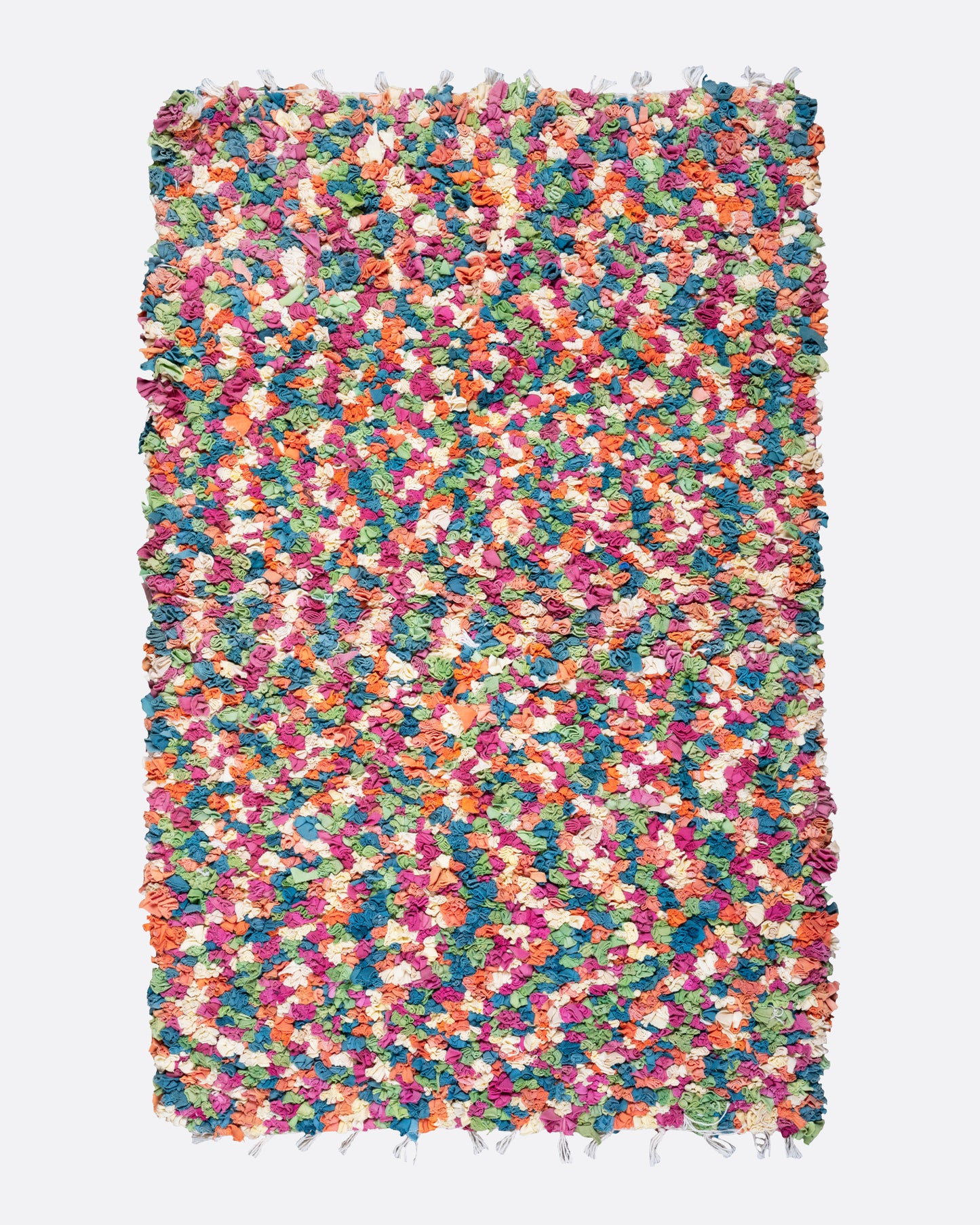 A bird's eye view of a green, red, orange, and white rectangular rag rug.