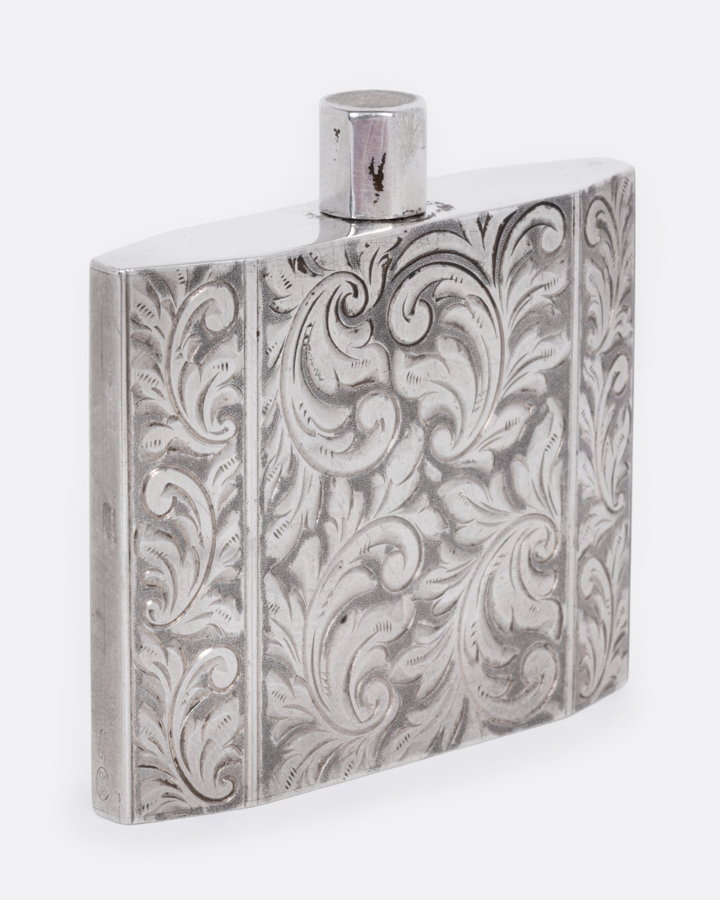 A silver perfume bottle with winding botanical etchings and a slim square silhouette, shown from the side.