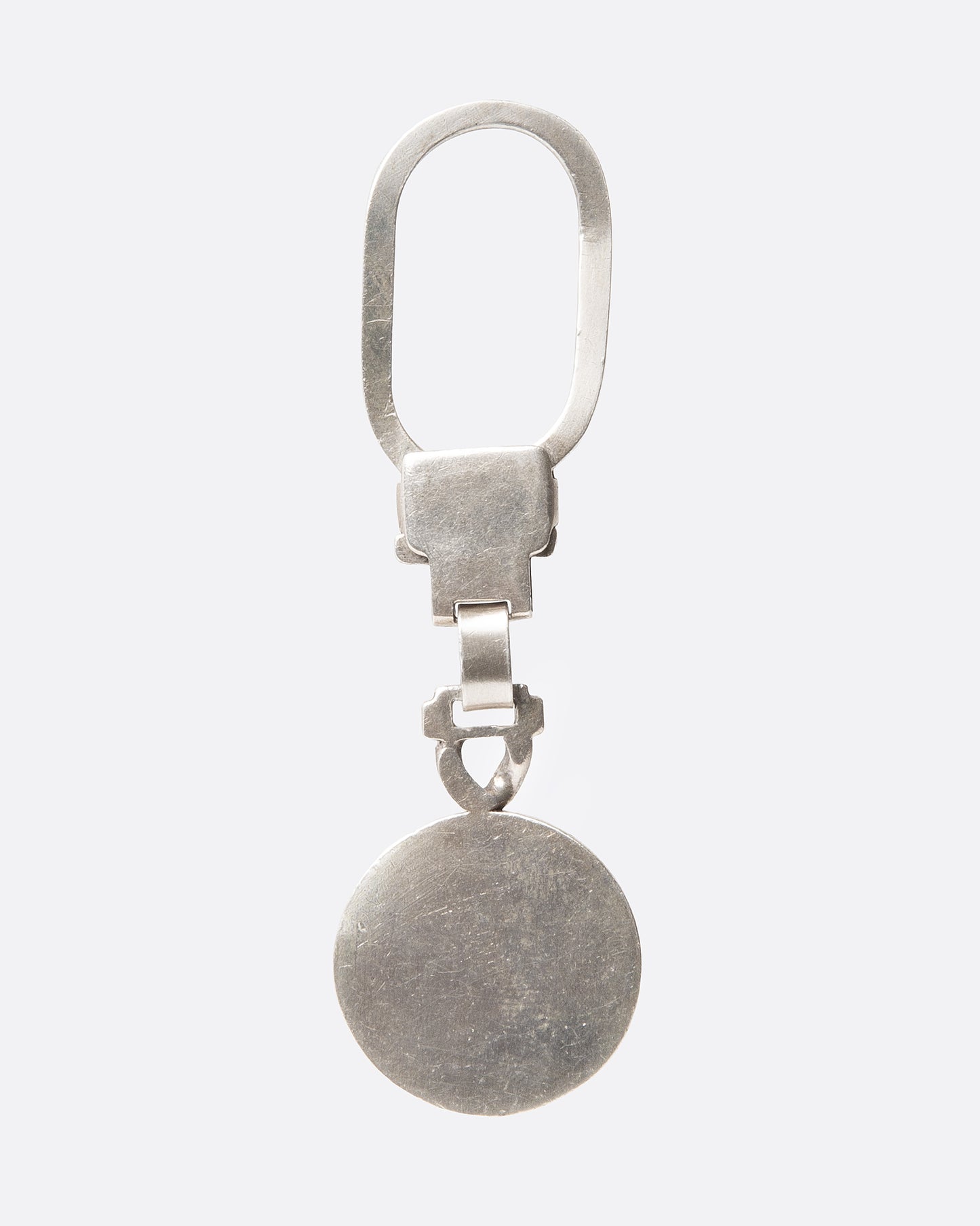 A silver key chain with a circular charm with engraved whiplash curves, shown from the back.