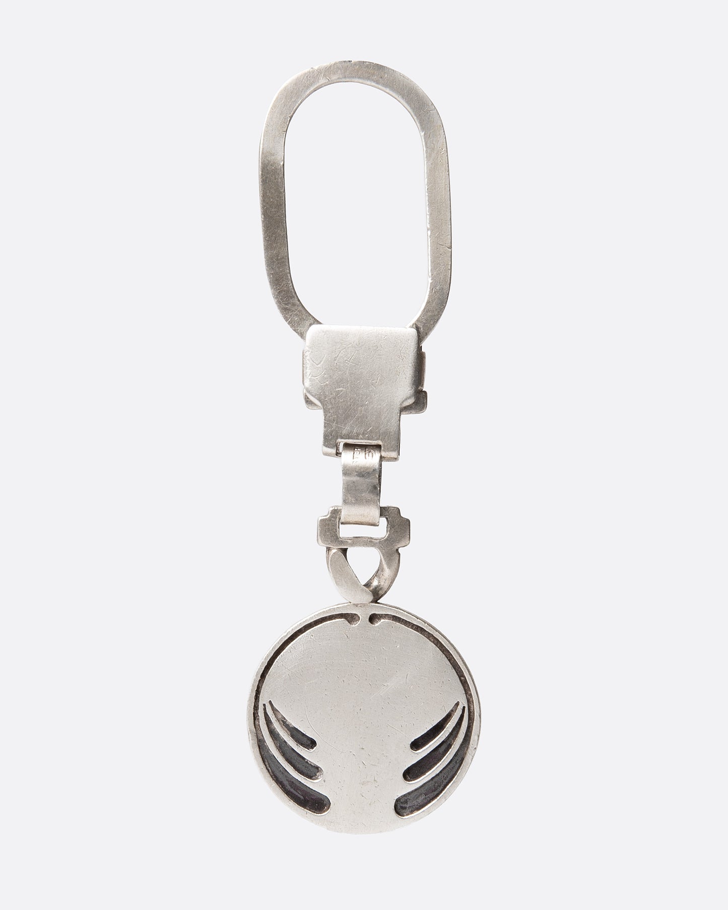 A silver key chain with a circular charm with engraved whiplash curves, shown from the front.