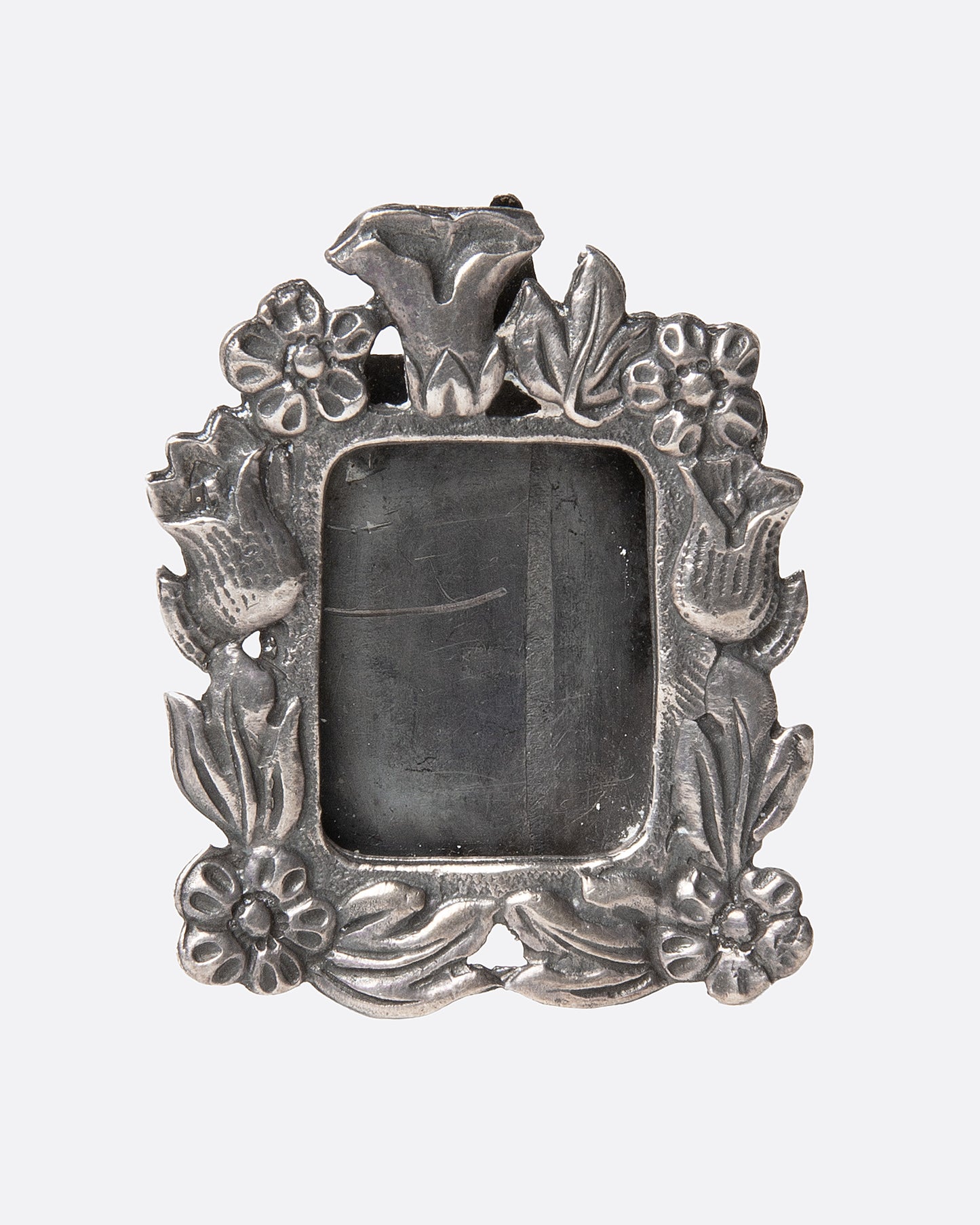 An ornate  silver picture frame brooch with a botanical motif around a rectangular opening, shown from the front.