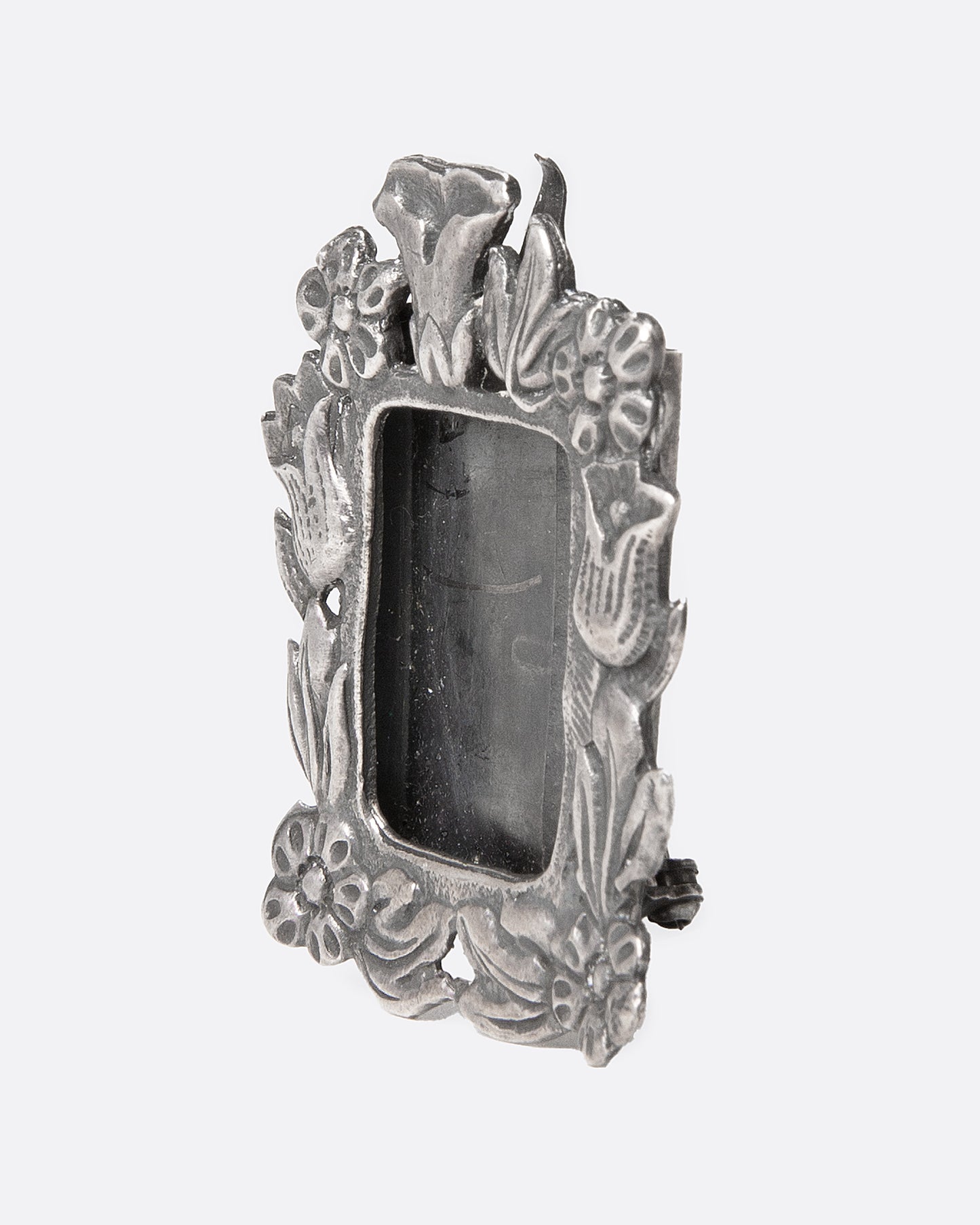 An ornate  silver picture frame brooch with a botanical motif around a rectangular opening, shown from the side.