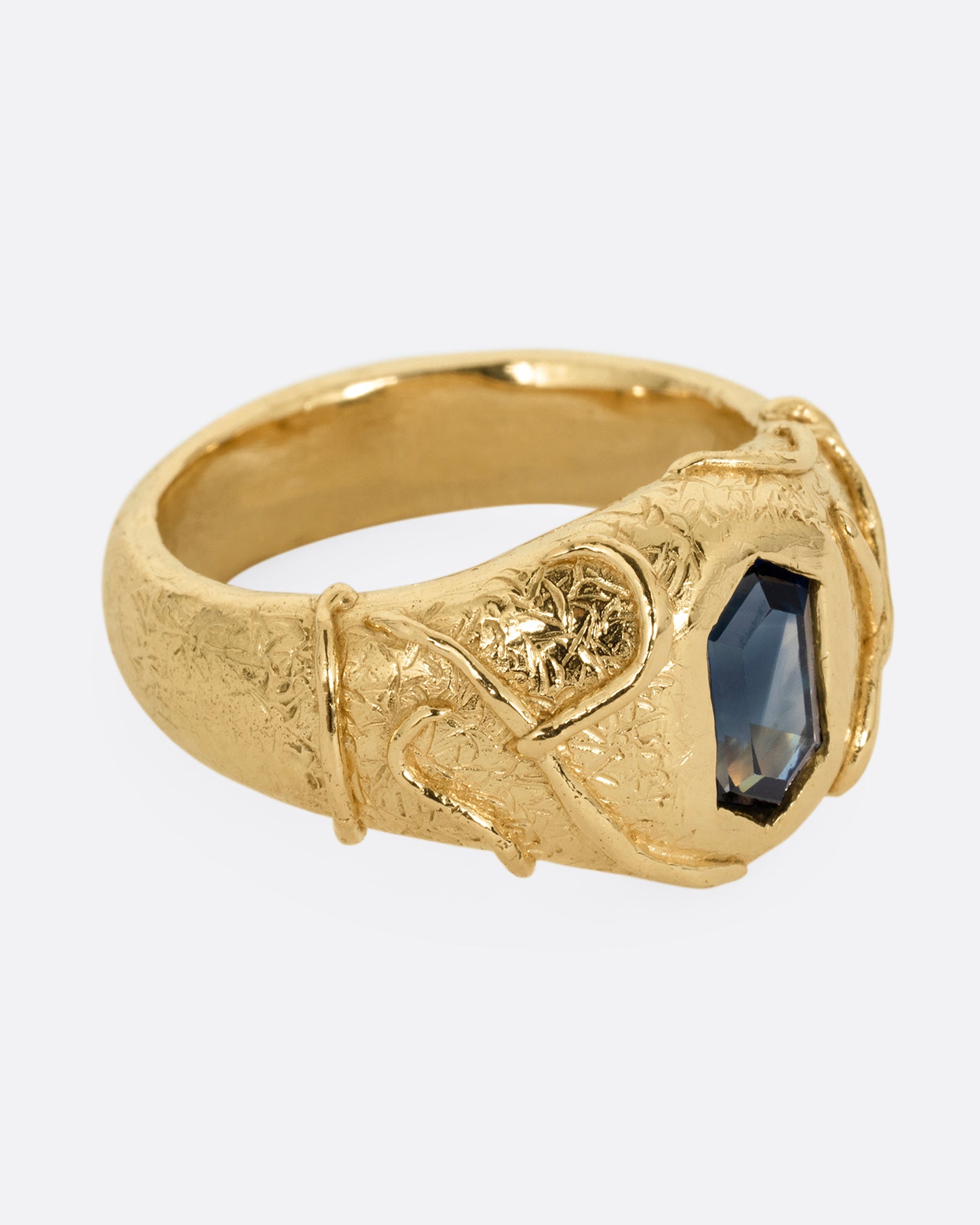 A yellow gold signet ring with a vine motif and a  hexagonal blue sapphire. Shown from the side.