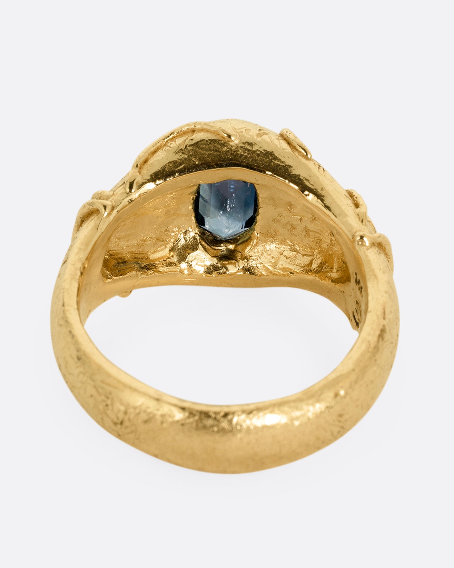 A yellow gold signet ring with a vine motif and a  hexagonal blue sapphire. Shown from the back.