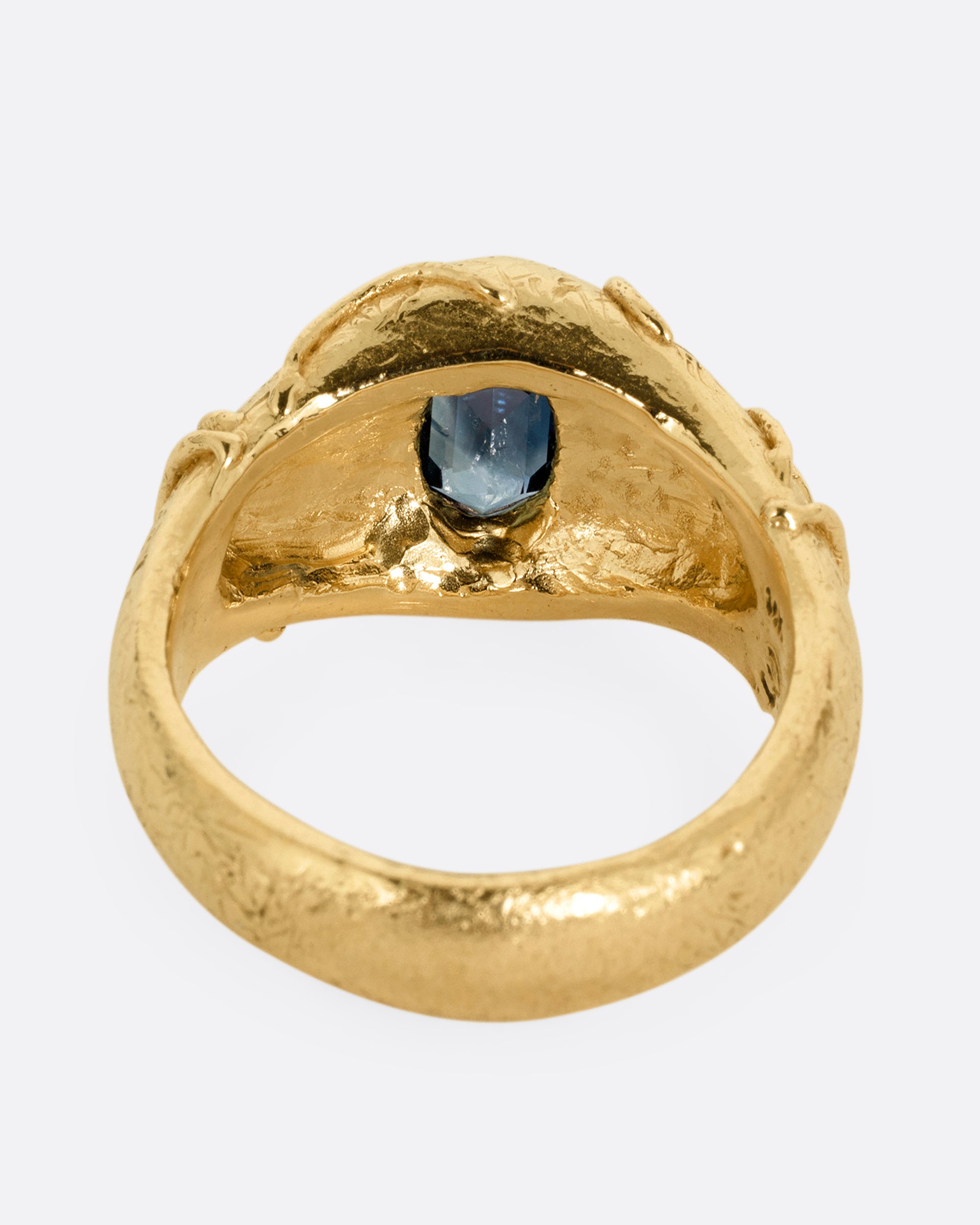 A yellow gold signet ring with a vine motif and a  hexagonal blue sapphire. Shown from the back.