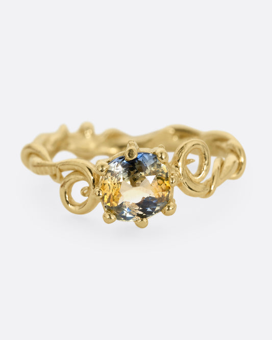A twisty yellow gold ring with a bicolor sapphire, shown from the front.