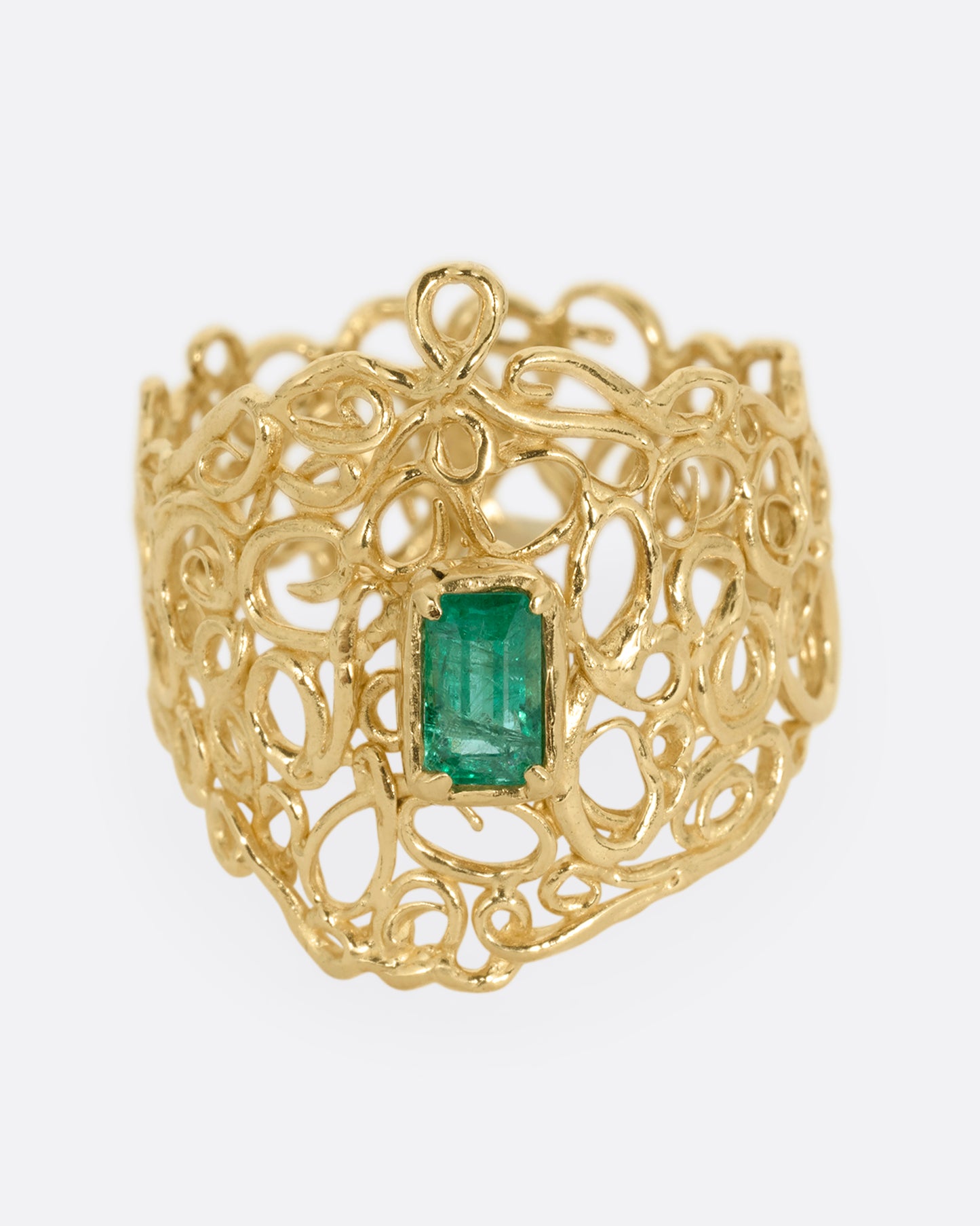 A wide yellow gold curling vine ring with  a central emerald. Shown from the front.