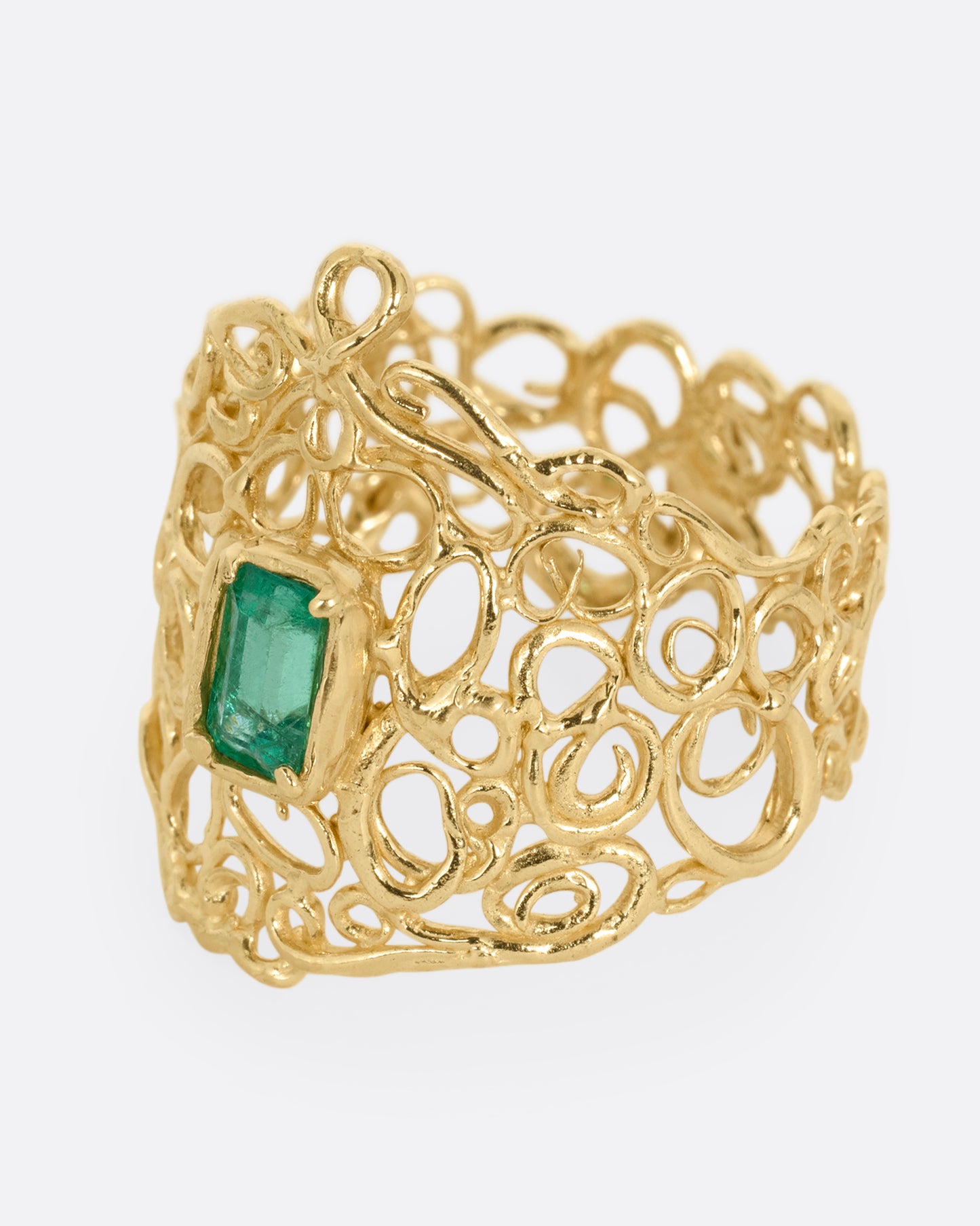 A wide yellow gold curling vine ring with  a central emerald. Shown from the side.