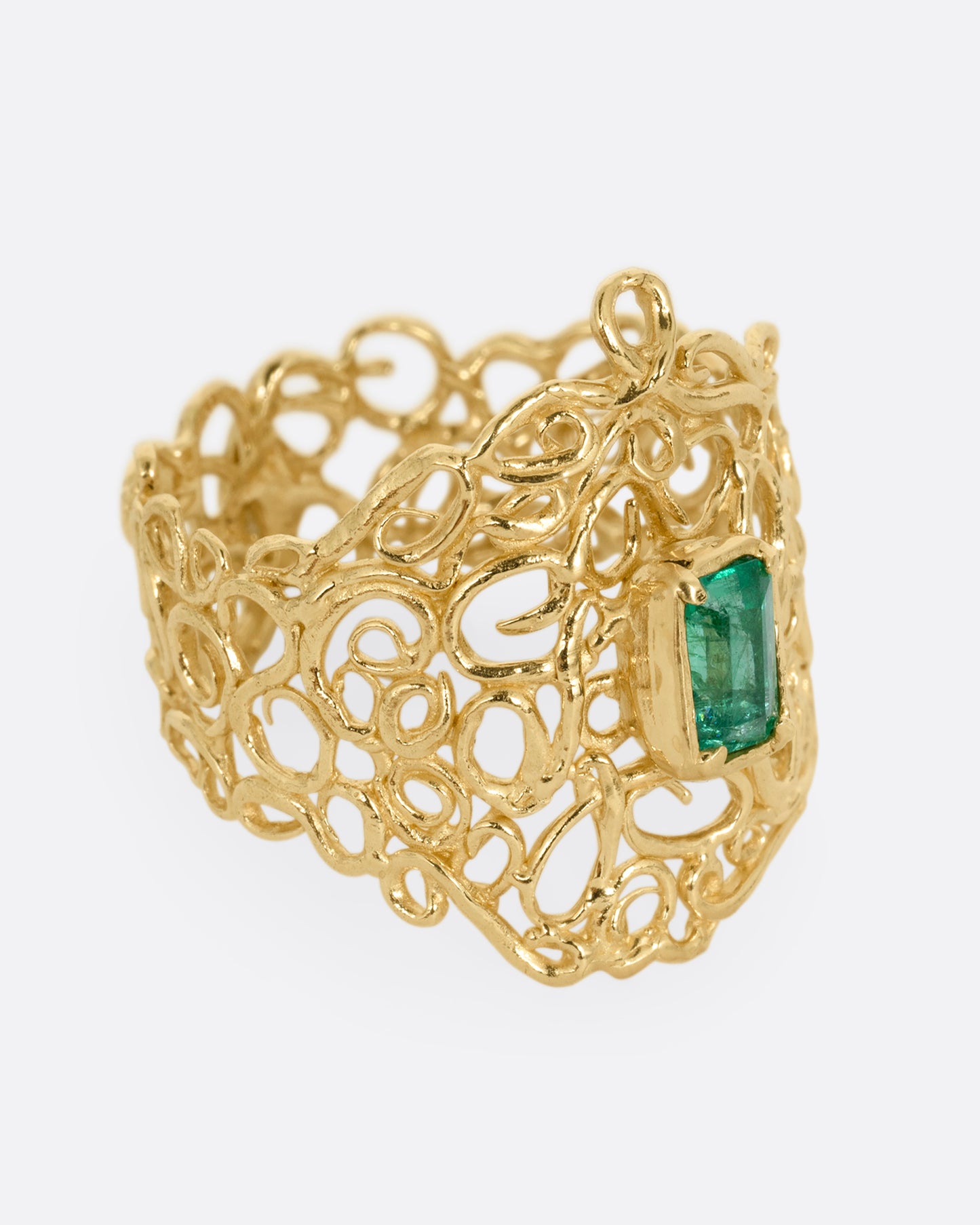 A wide yellow gold curling vine ring with  a central emerald. Shown from the side.