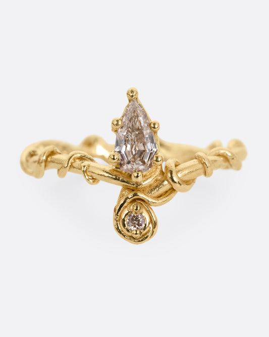 A yellow gold ring with a vine wrapped band and two stacked diamonds, one pear one round. Shown from the front.