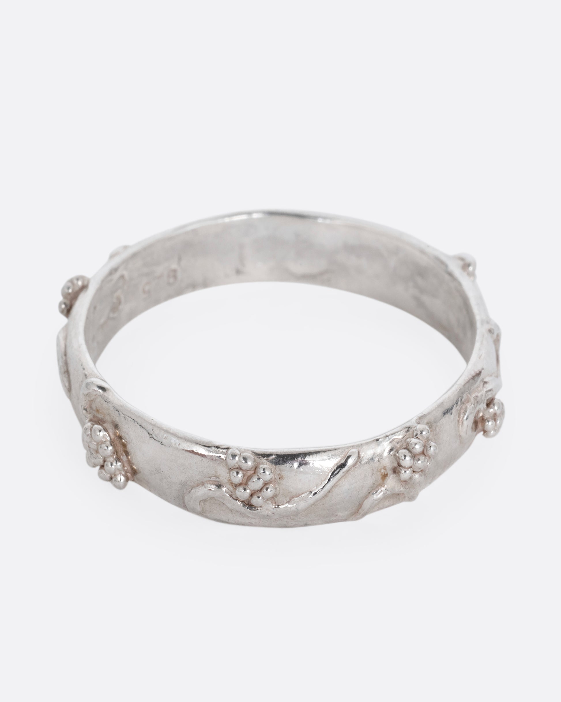 A silver ring with a grape vine motif. Shown from the front.