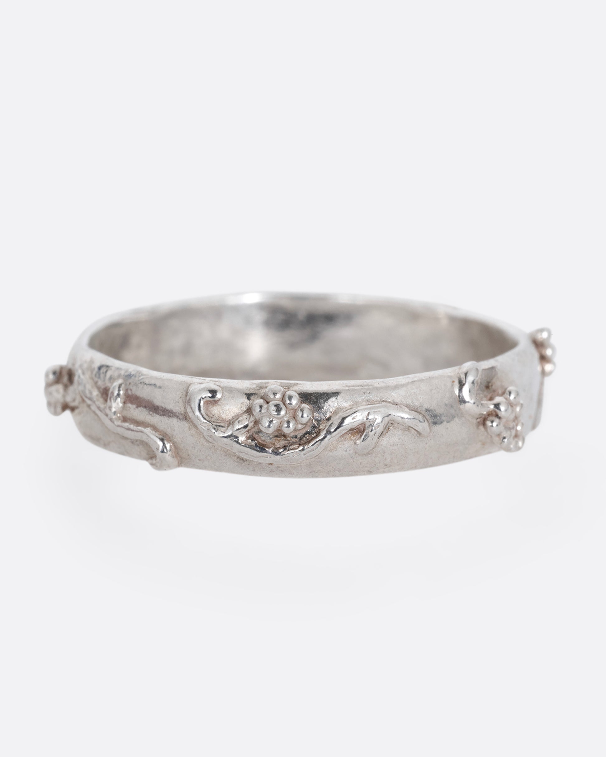 A silver ring with a grape vine motif. Shown from the front.