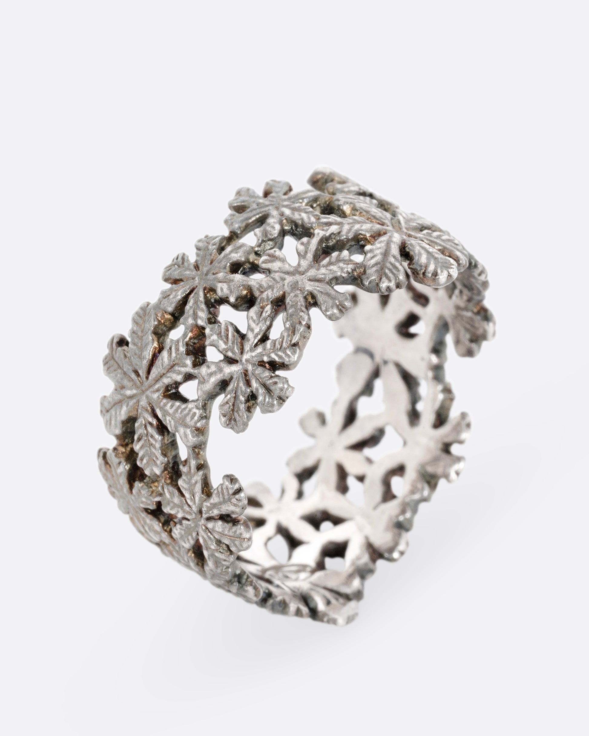 A wide silver ring with a pattern of flowers, shown standing up from the front.