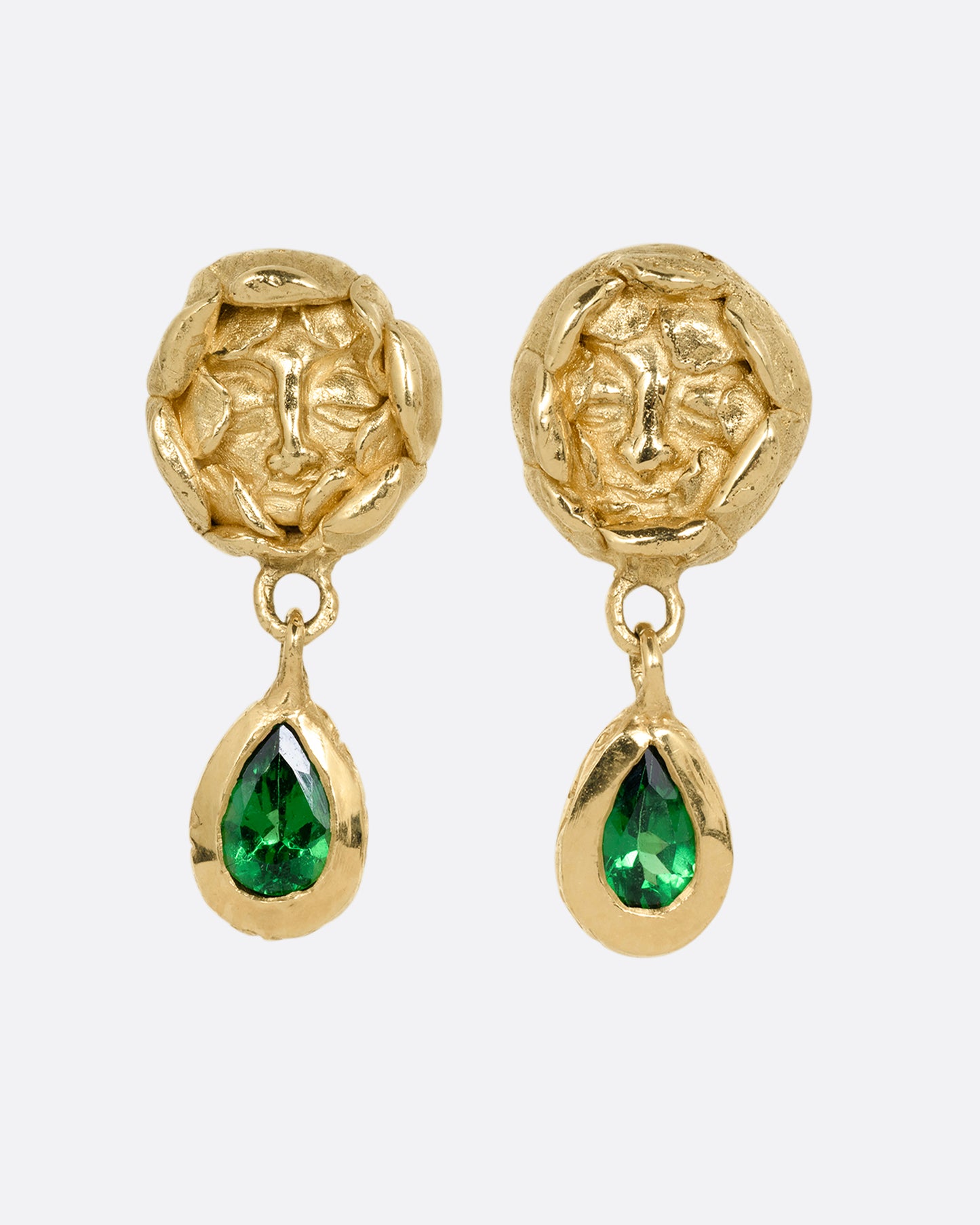 A pair of yellow gold studback earrings with faces at the center of rosebuds and a pear shaped tsavorite dangle. Shown from the front.