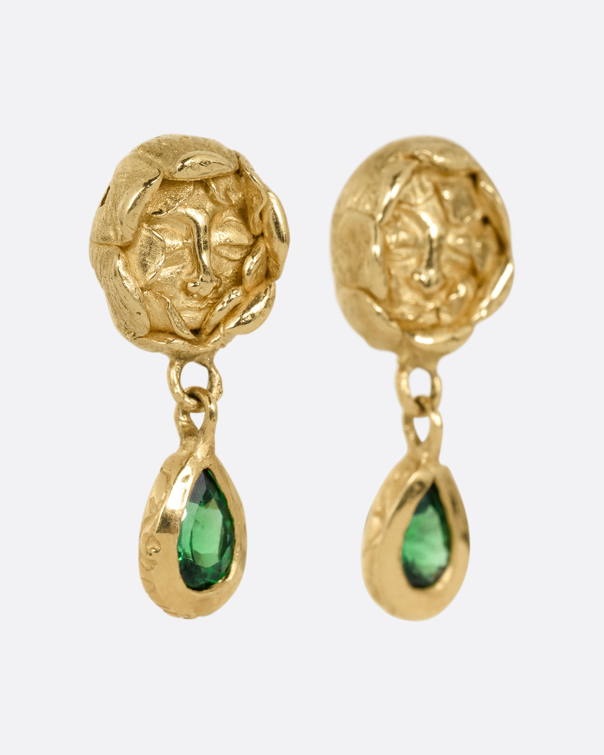 A pair of yellow gold studback earrings with faces at the center of rosebuds and a pear shaped tsavorite dangle. Shown from the side.