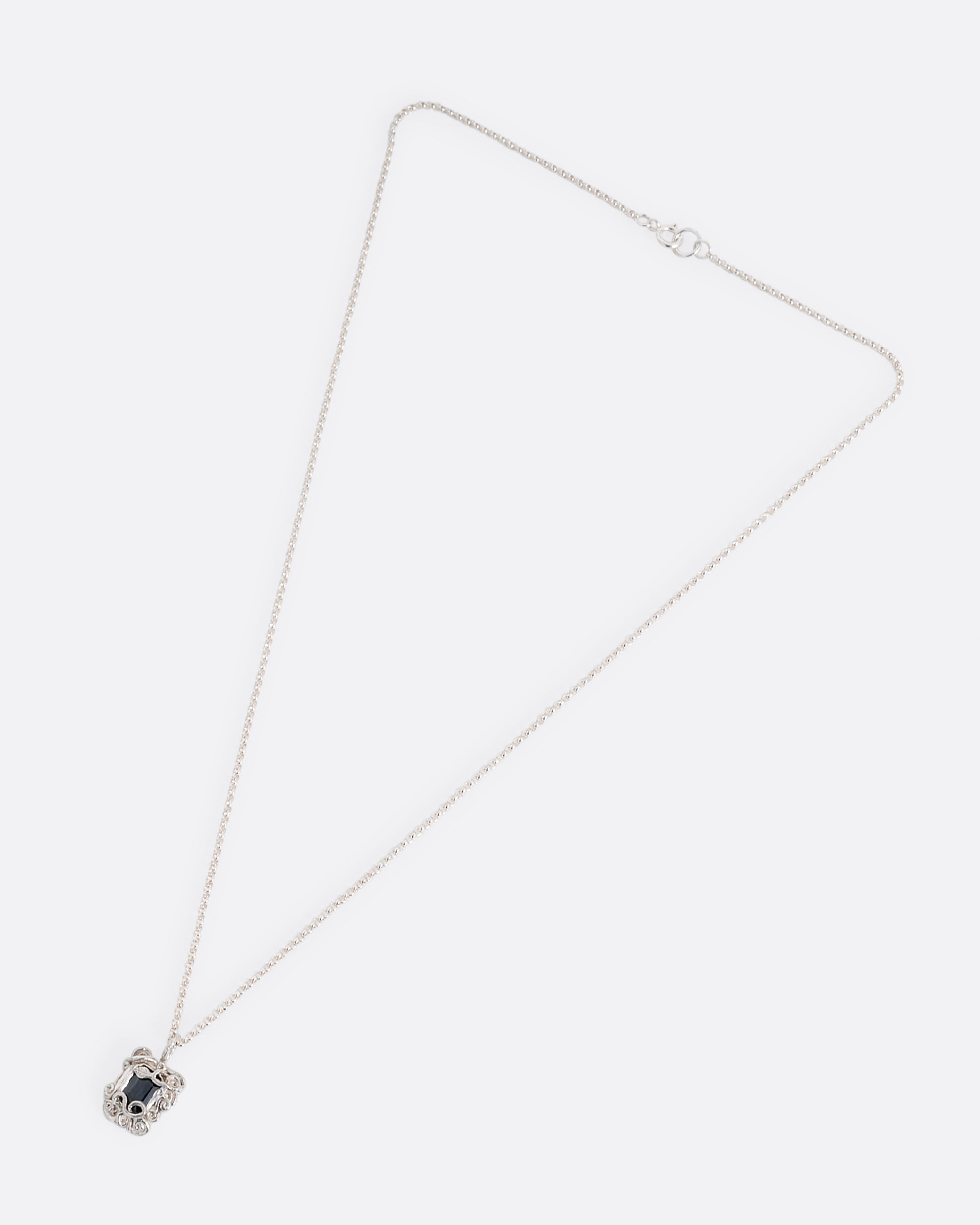 A silver pendant necklace with a deep blue sapphire in a setting with creeping vines. Shown from the front.