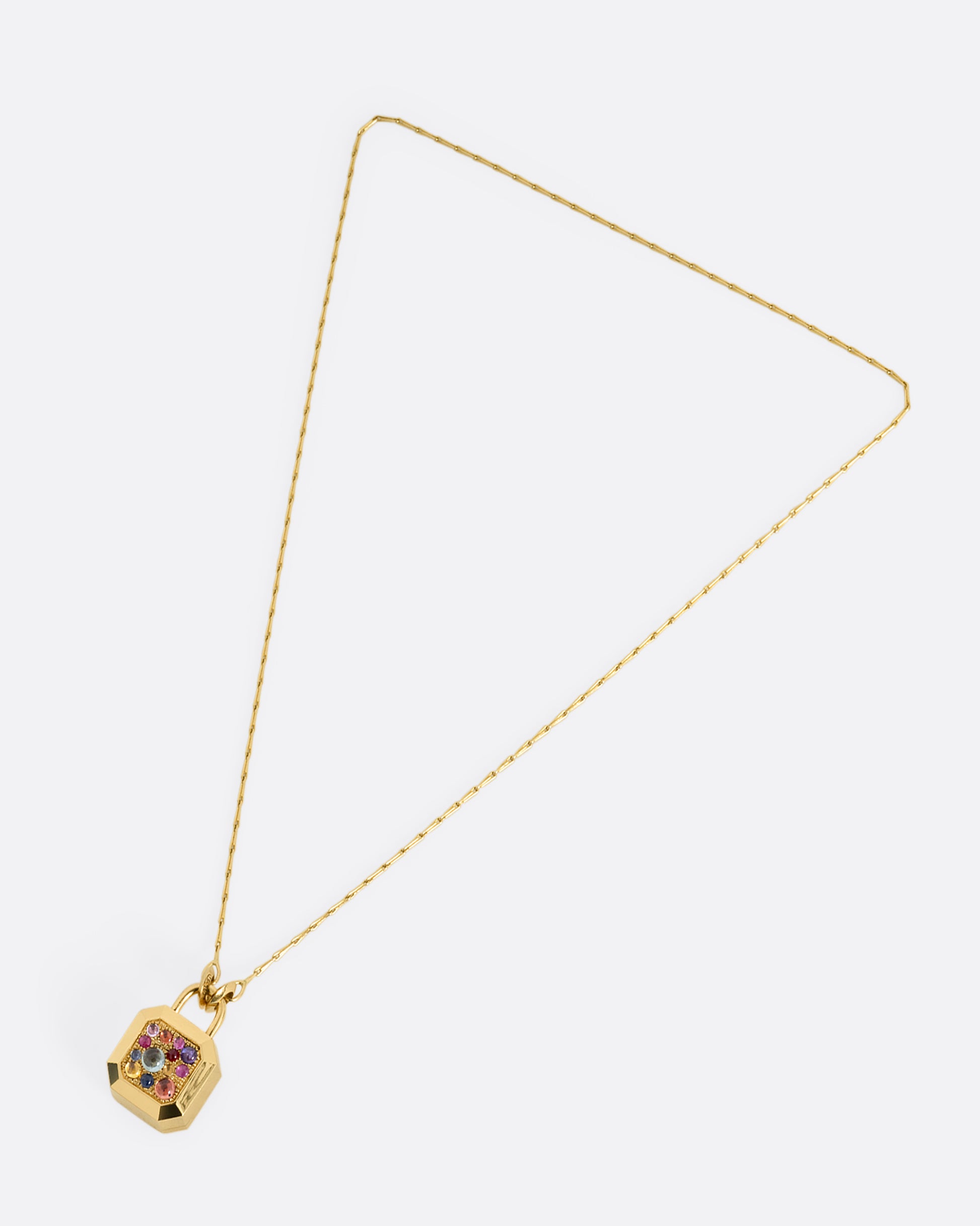 A yellow gold necklace with a padlock shaped locket pendant with multicolored sapphire on its face. Shown from the front.