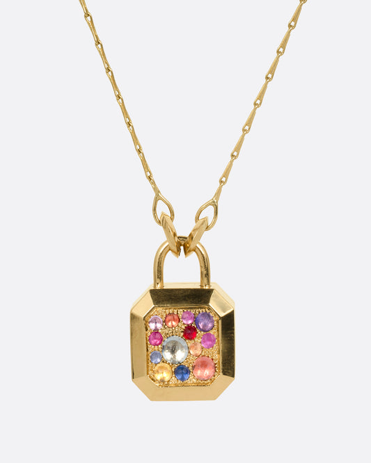 A yellow gold necklace with a padlock shaped locket pendant with multicolored sapphire on its face. Shown from the front.
