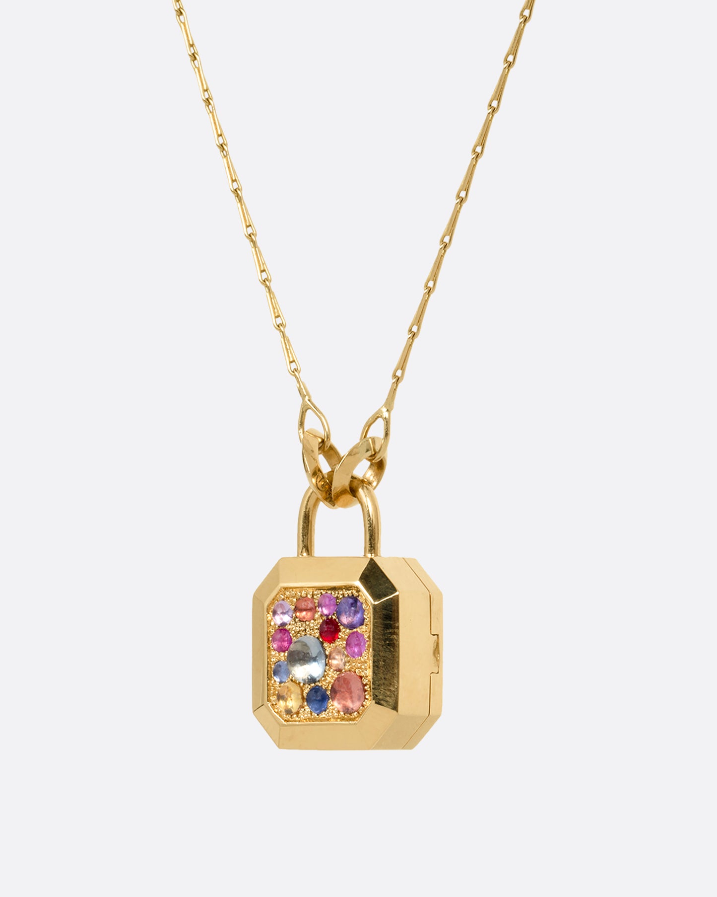 A yellow gold necklace with a padlock shaped locket pendant with multicolored sapphire on its face. Shown from the side.