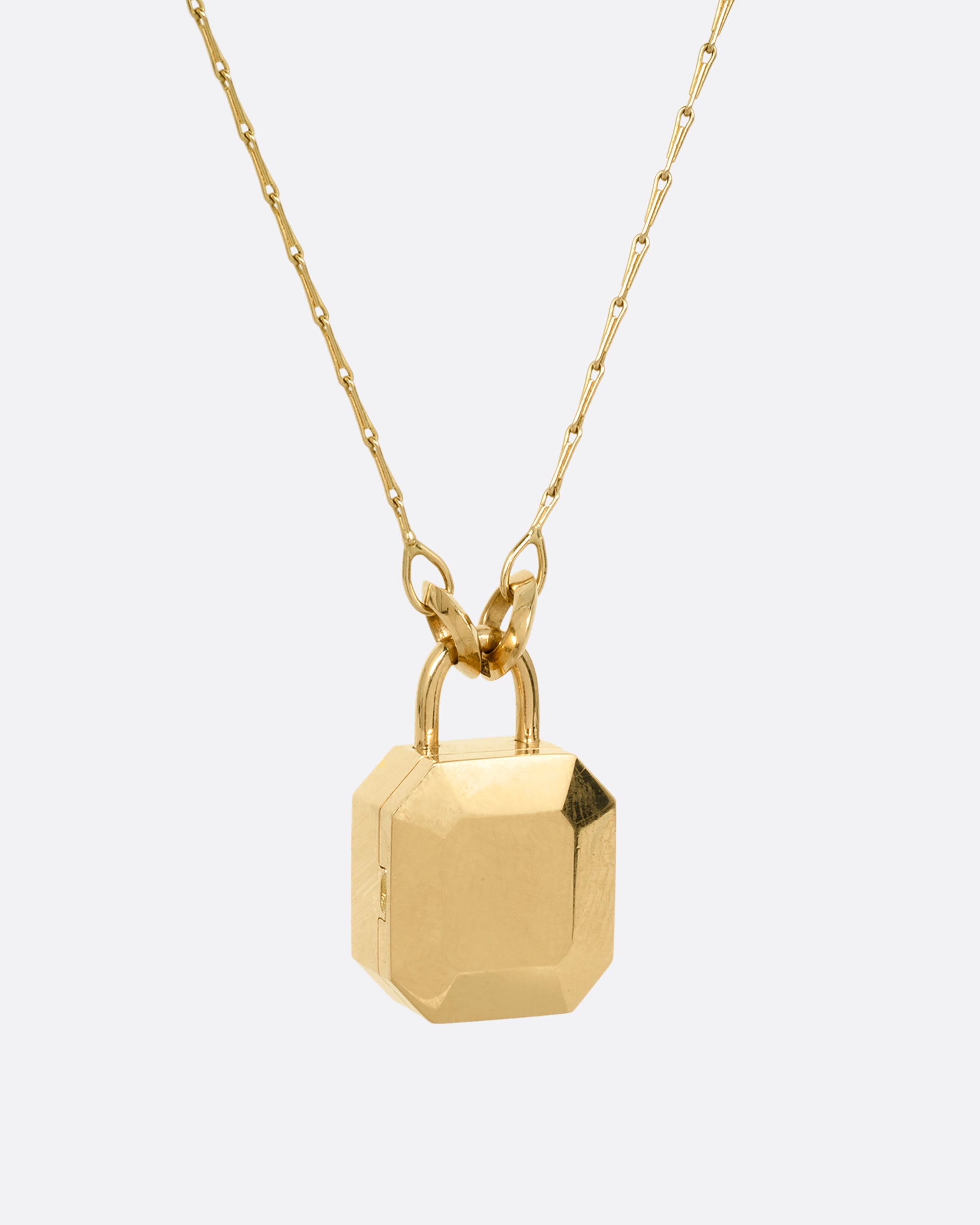 A yellow gold necklace with a padlock shaped locket pendant with multicolored sapphire on its face. Shown from the back.