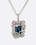 A silver pendant necklace with a deep blue sapphire in a setting with creeping vines. Shown from the front.
