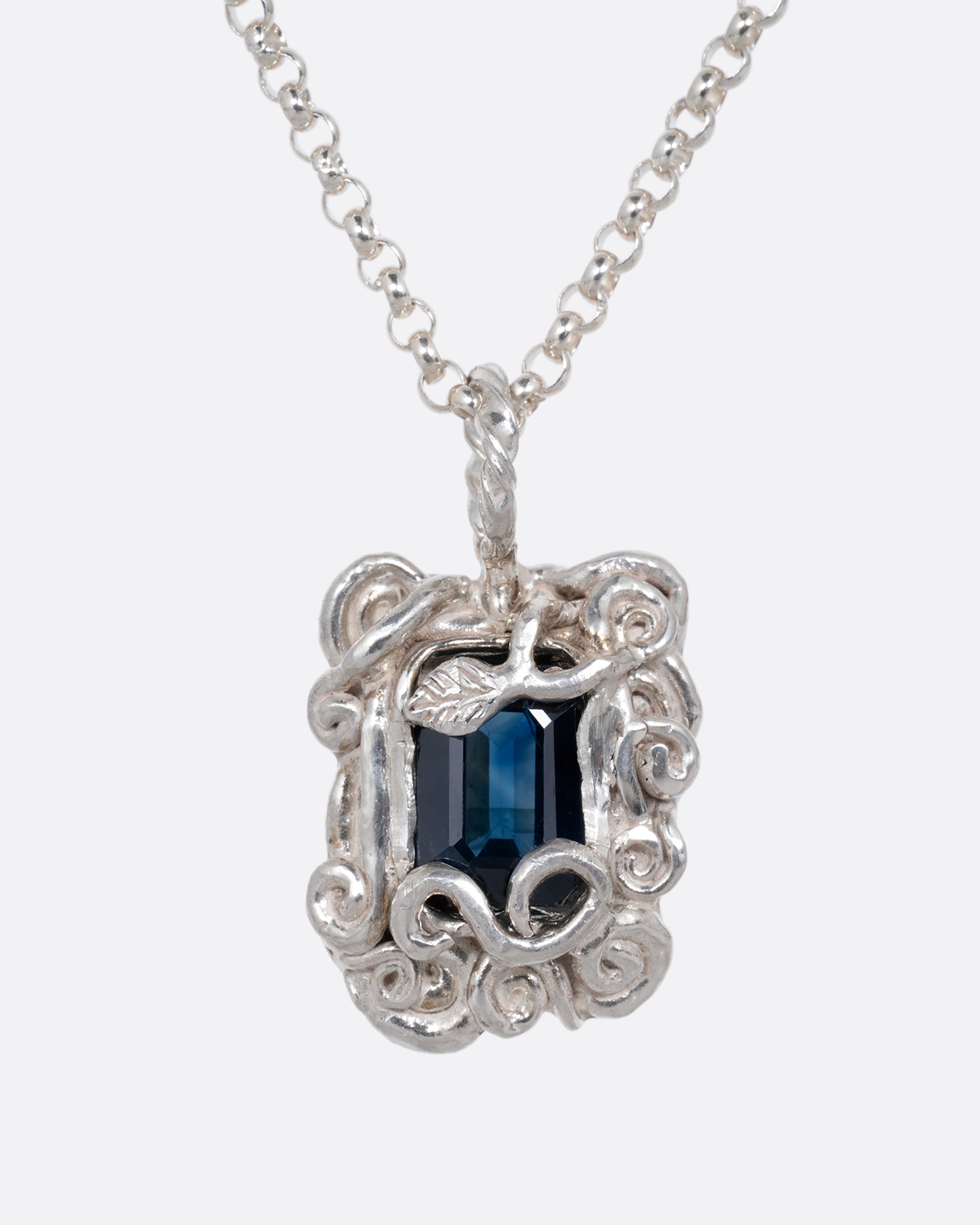 A silver pendant necklace with a deep blue sapphire in a setting with creeping vines. Shown from the front.