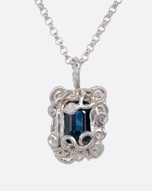 A silver pendant necklace with a deep blue sapphire in a setting with creeping vines. Shown from the front.