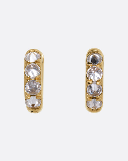 A pair of yellow gold huggie hoop earrings, each set with reverse set diamonds, shown from the front.