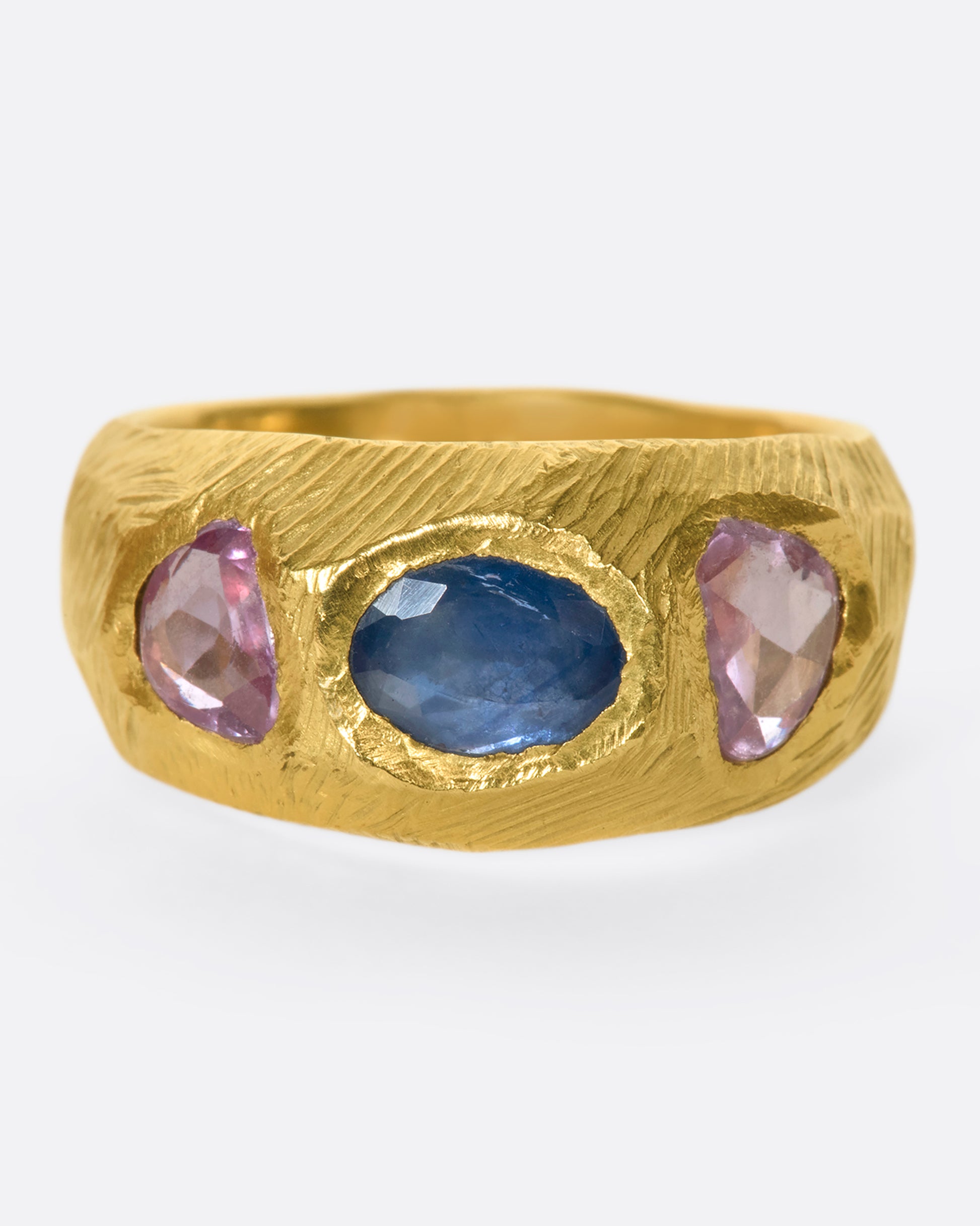 This hand carved 18k gold band is inlaid with an oval blue sapphire, flanked by beautiful pink sapphires