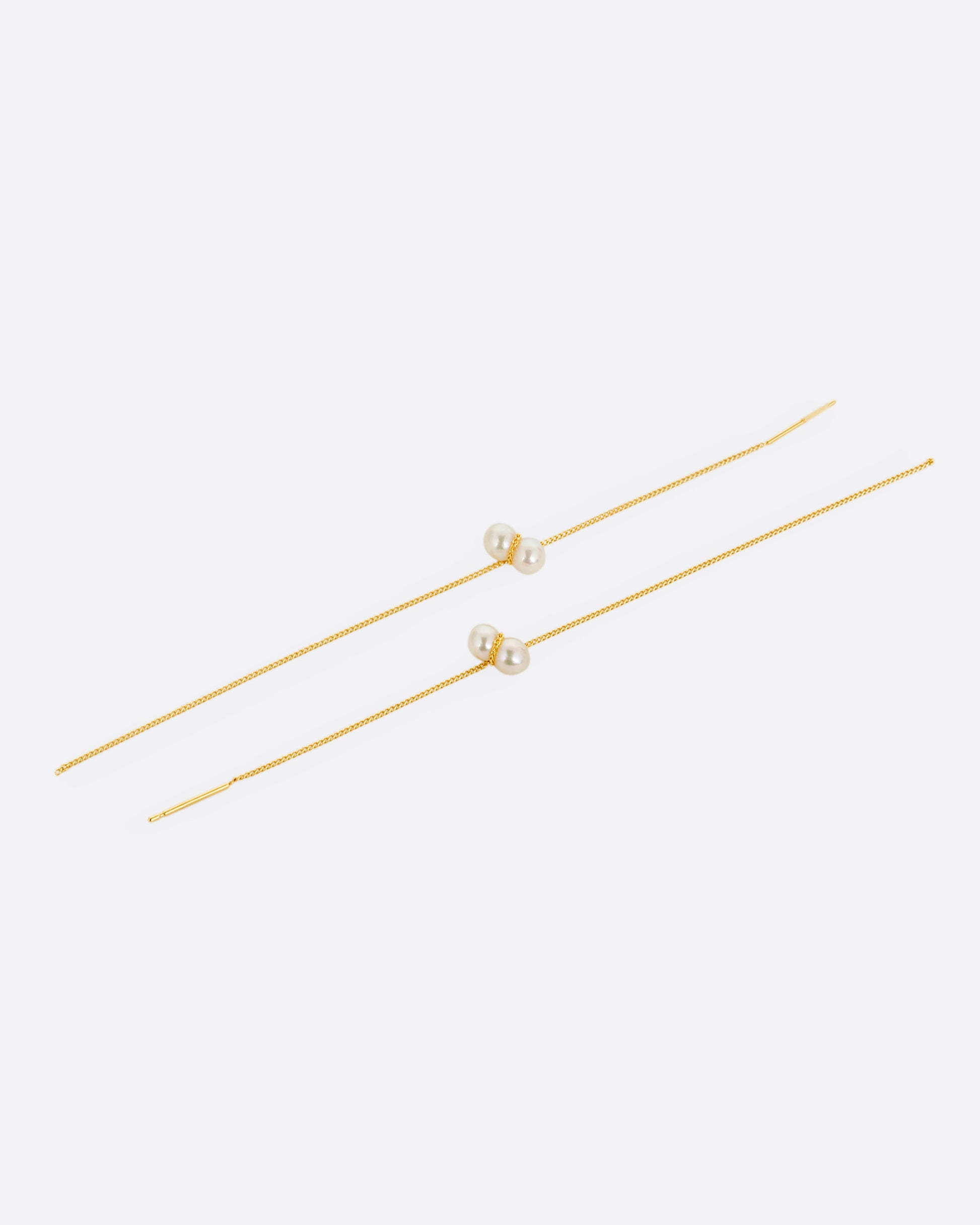 Two yellow gold cable chain threader earrings with white pearls, shown lying flat.
