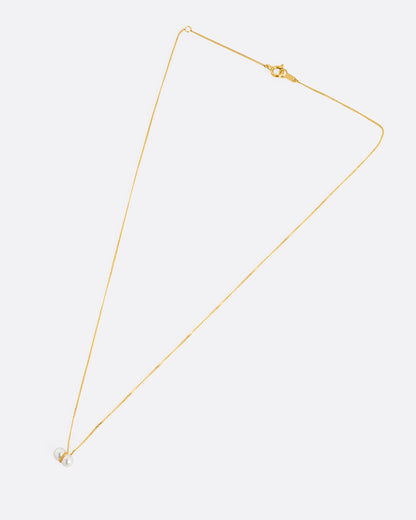 A yellow gold necklace with a small double pearl pendant. Shown laying flat.