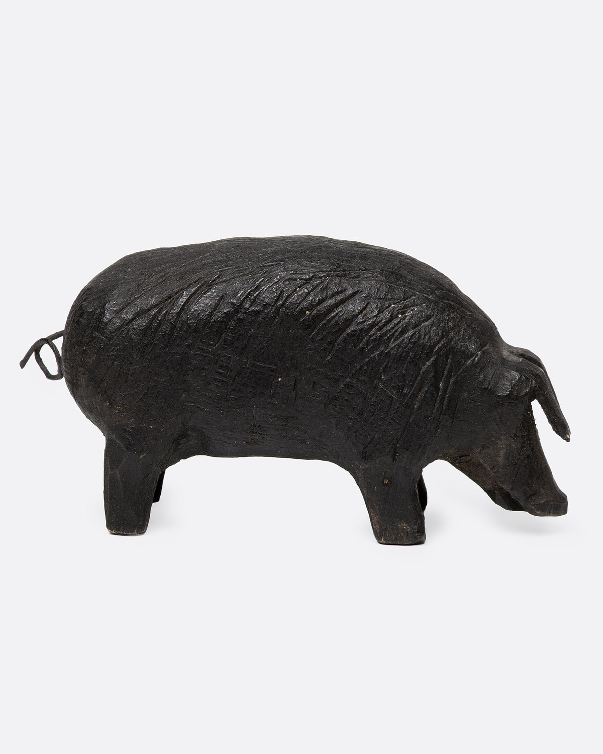 A wooden hand carved pig figurine with a wire tail, shown from the side.