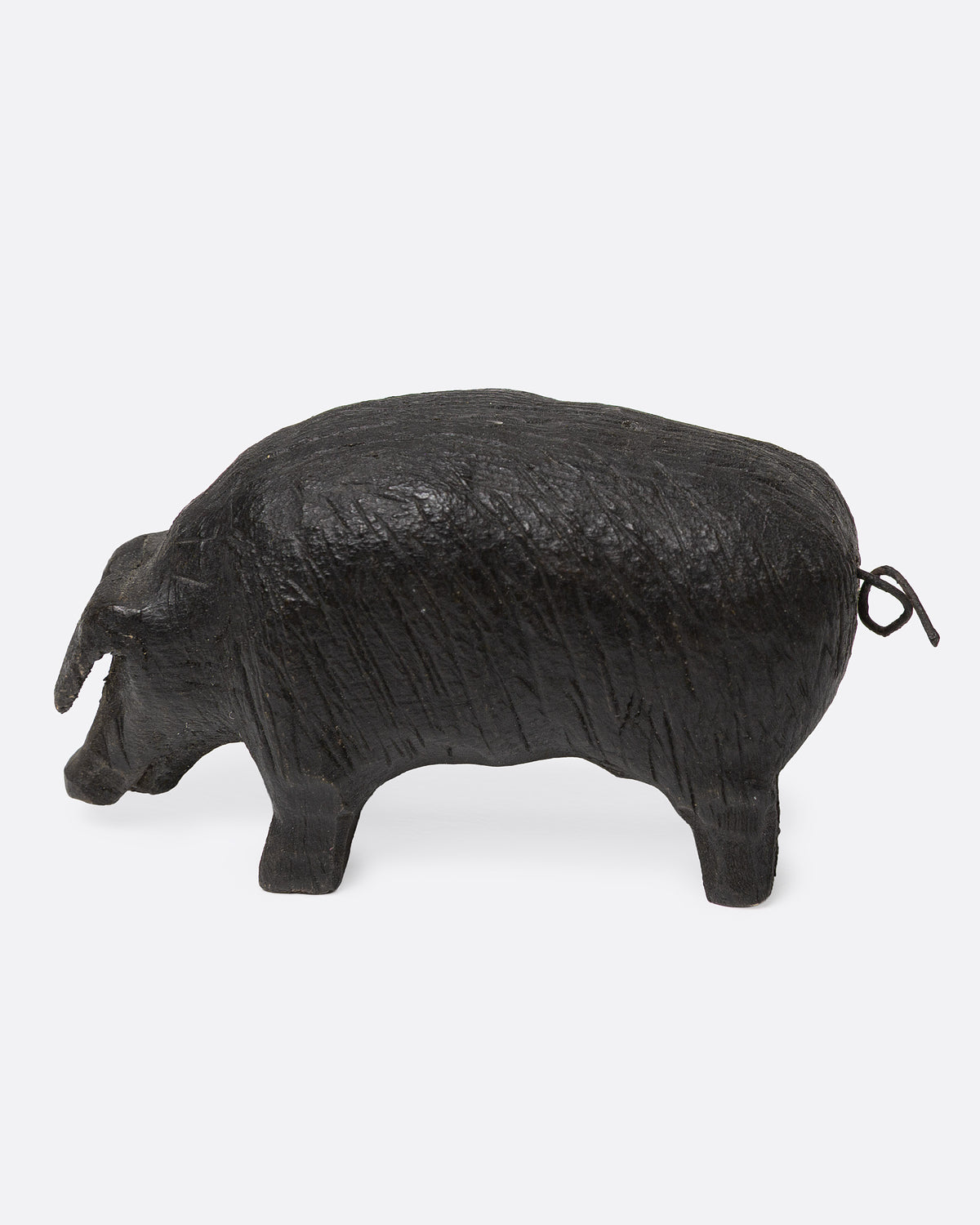 A wooden hand carved pig figurine with a wire tail, shown from the side.