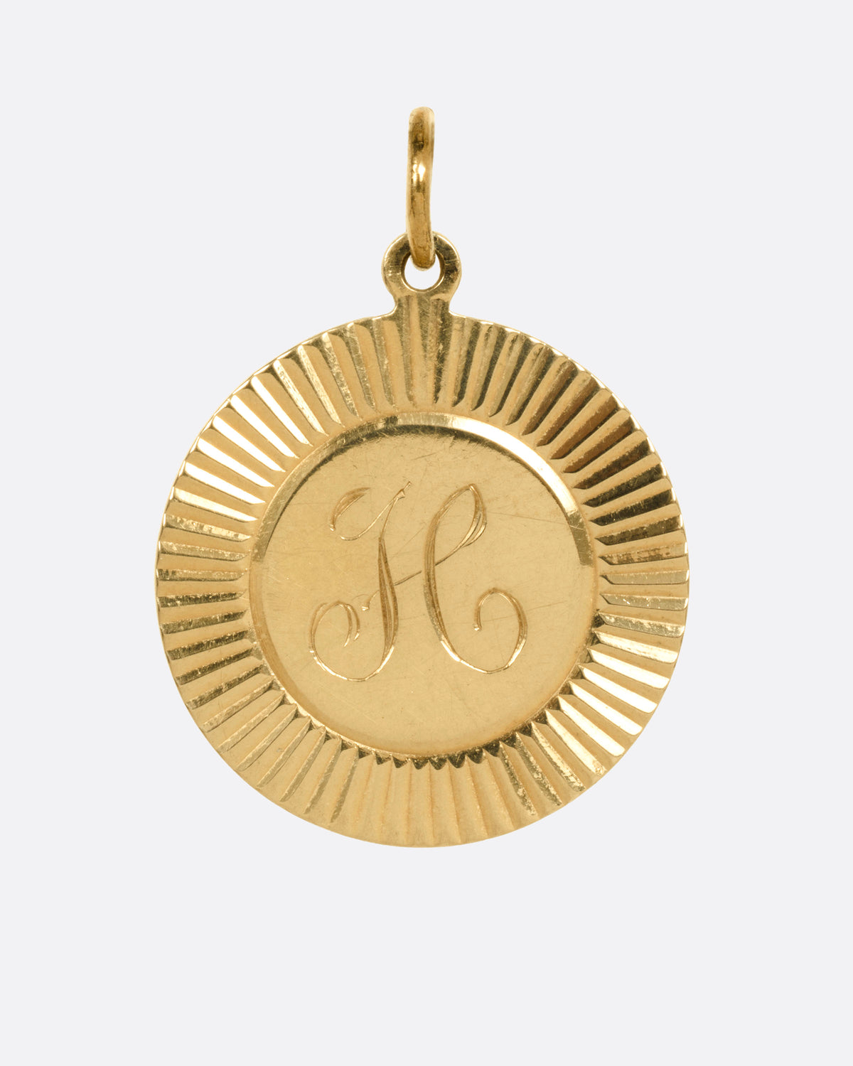 A round gold pendant with a sunburst radiating from a central engraved letter 'H', shown from the front.