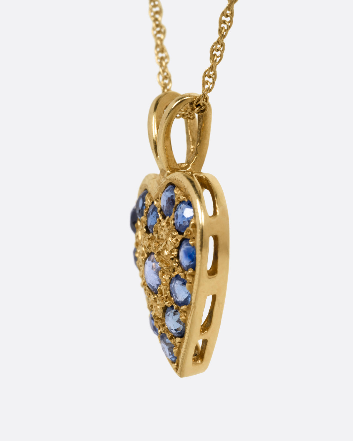 A yellow gold necklace with a heart shaped pendant with blue sapphires, shown from the side.