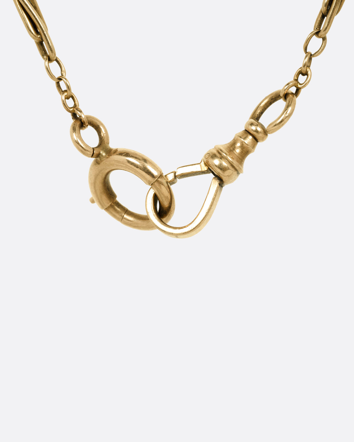 A close up of a yellow gold clasp on a Victorian watch chain necklace.